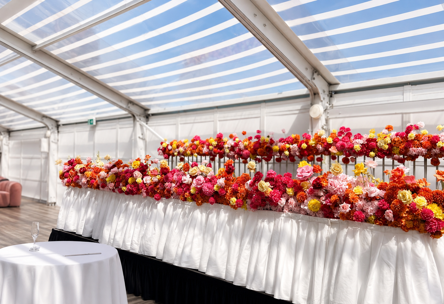 Colorful flower arrangements on a long table in a bright event space with a striped ceiling.