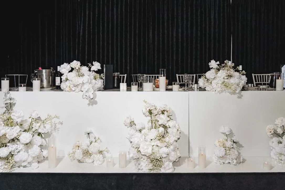 Table decorated with white flower arrangements and candles at a wedding or event venue.