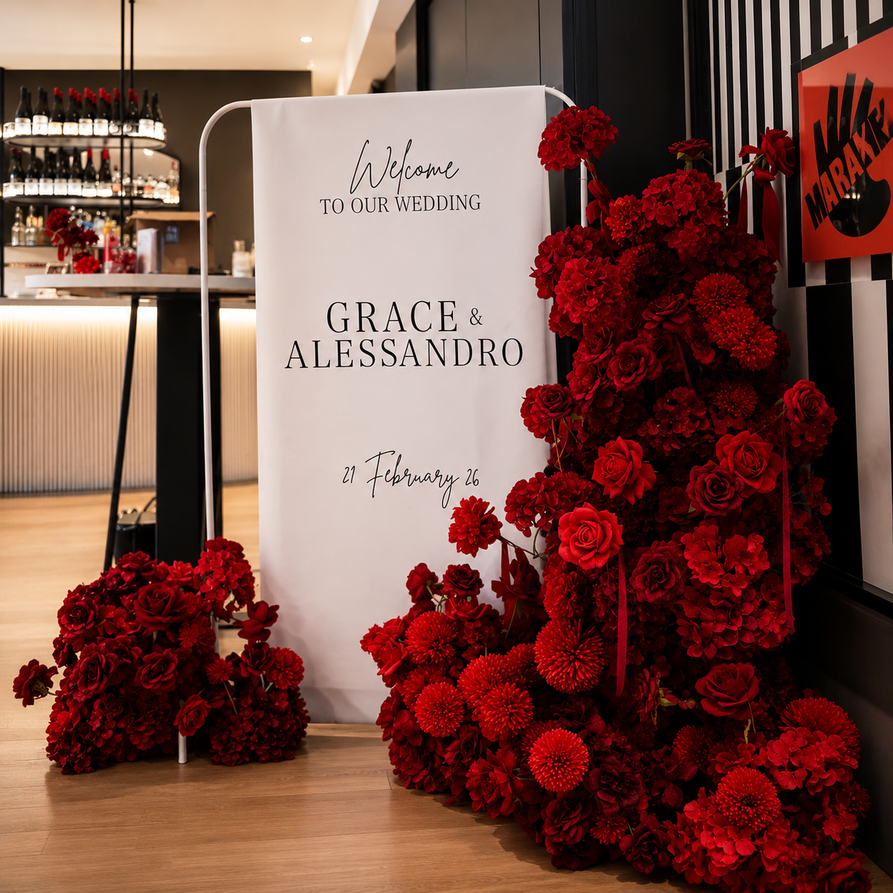 Wedding welcome sign with red floral arrangements on a wooden floor in a modern indoor setting.