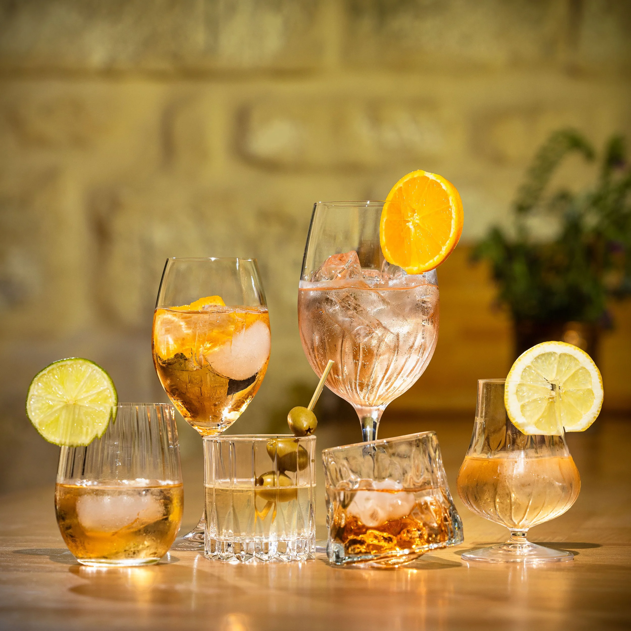 Plusieurs verres à cocktail avec des tranches de citron, lime, orange et des glaçons, posés sur une surface en bois.