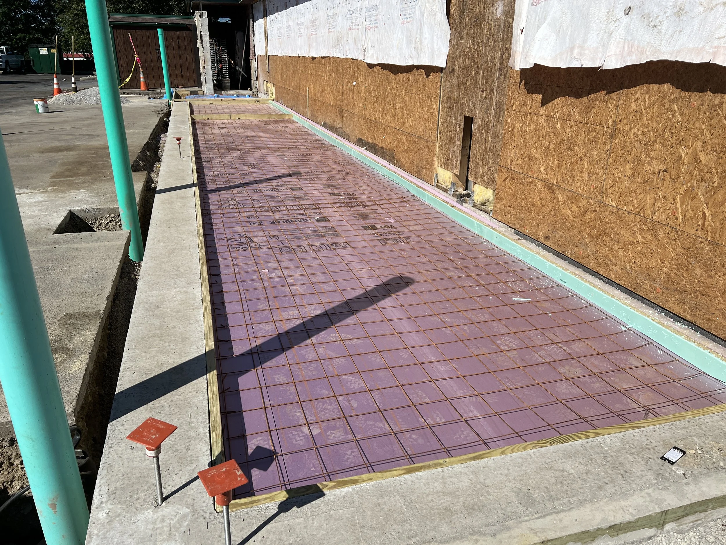 Construction site with for a new Texas Roadhouse freezer addition before the slab pour after inspection, orange traffic cones, and plywood wall with insulation, showing ongoing renovation.