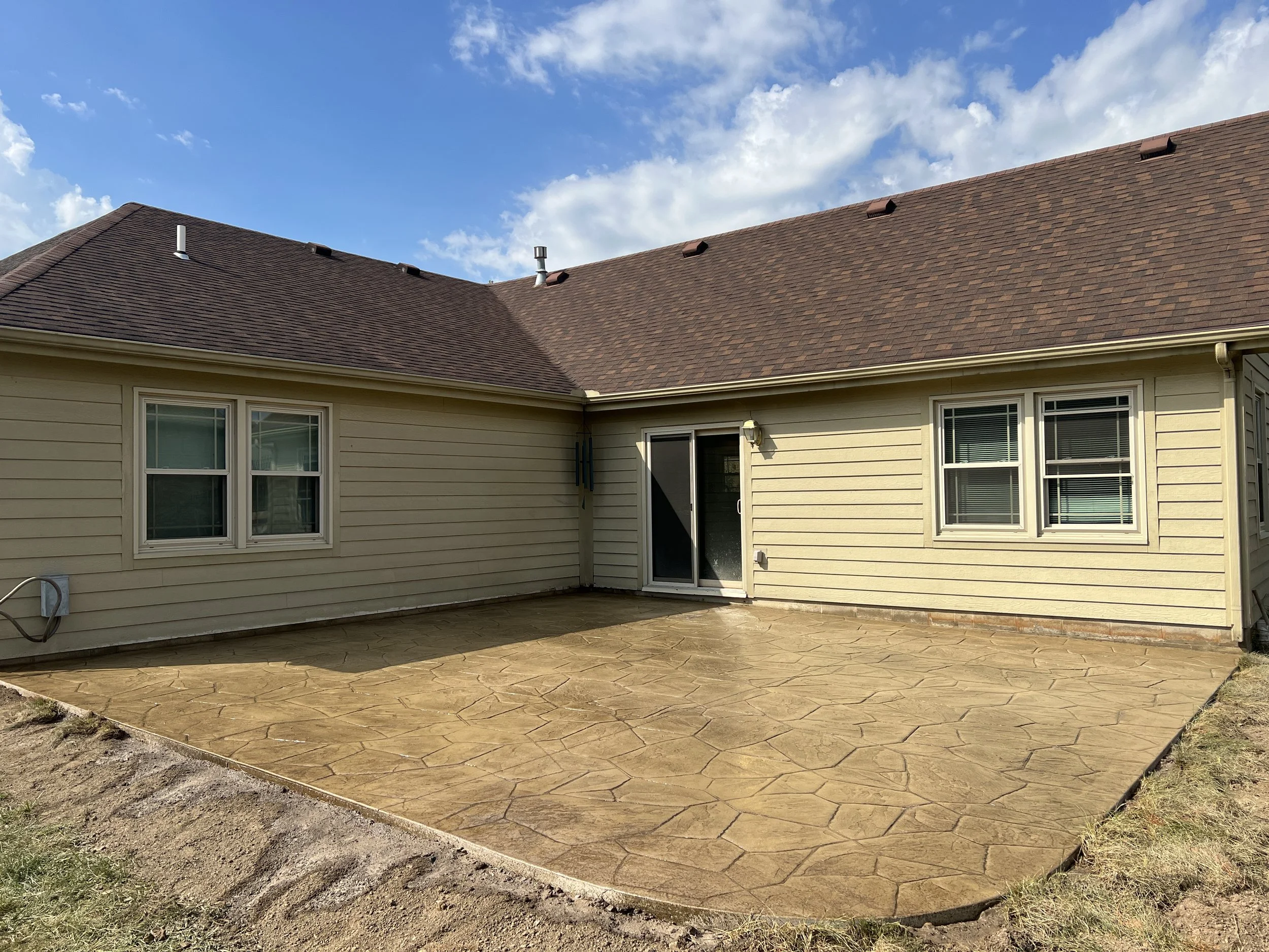 Backyard freshly sealed stamped concrete paved patio area under a partly cloudy sky.