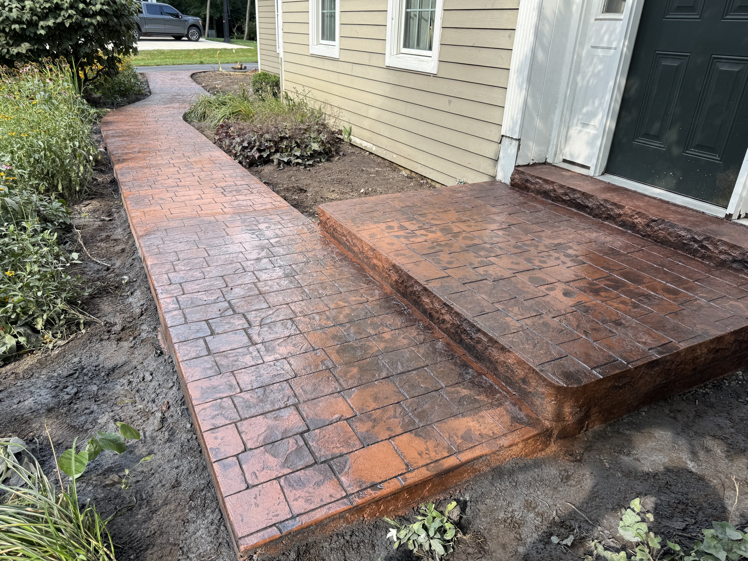 Newly installed red brick Stamped Concrete walkway leading to the front door of the home, with form work removed and backfilled.