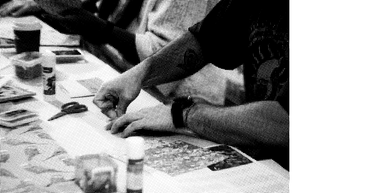 A person working on an art or craft project at a table, surrounded by various small objects, tools, and supplies.