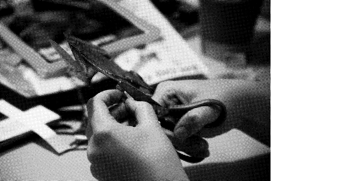 Black and white photograph of a person cutting out some paper with small scissors, surrounded by scattered cut paper.