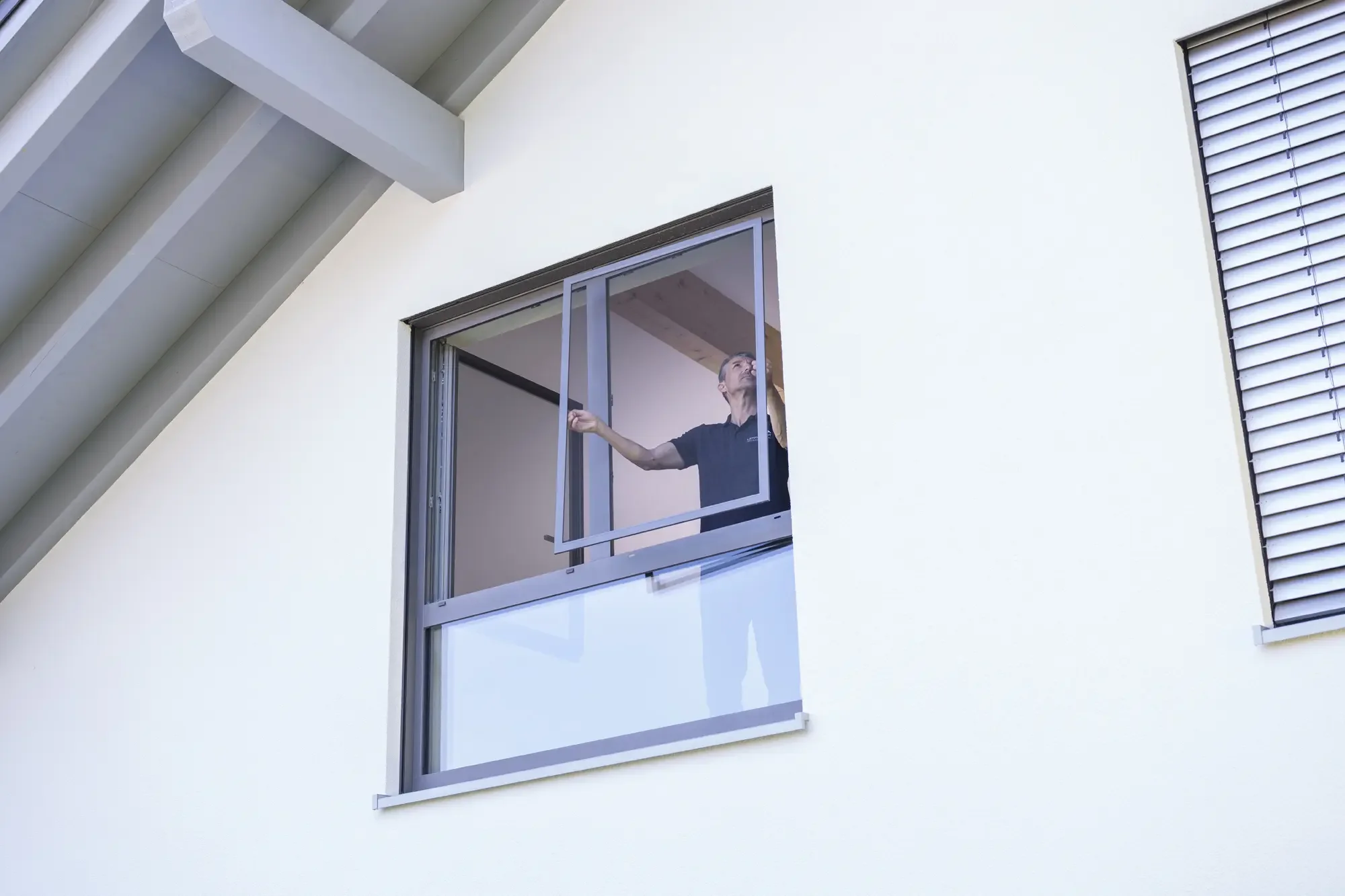 Mann öffnet ein Fenster in einem modernen weißen Gebäude.