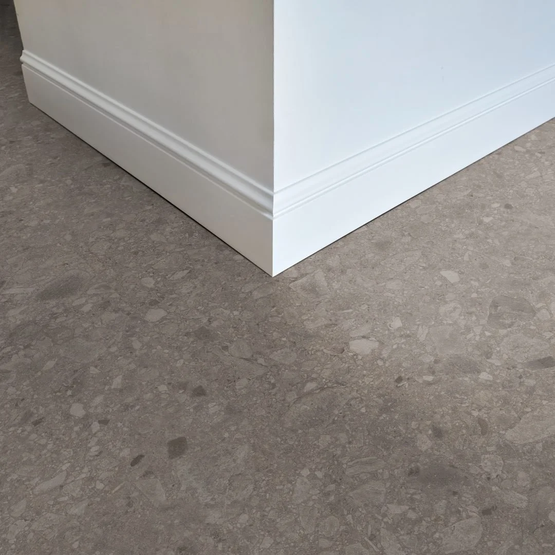 Nahaufnahme einer Wand mit Sockelleiste auf einem grauen Terrazzoboden. 