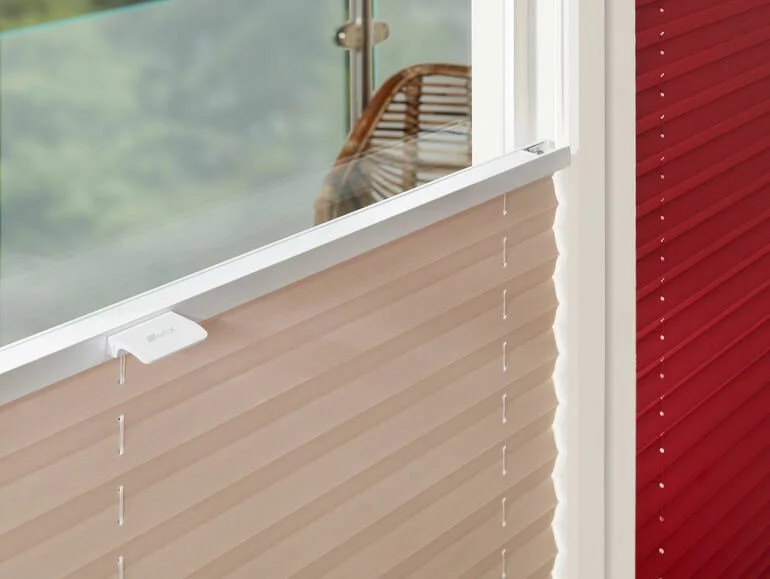 Innenansicht eines Fensters mit beige- und rotfarbenen Jalousien, Blick nach draußen auf eine grüne Landschaft, auf der Fensterbank ein WLAN-Adapter