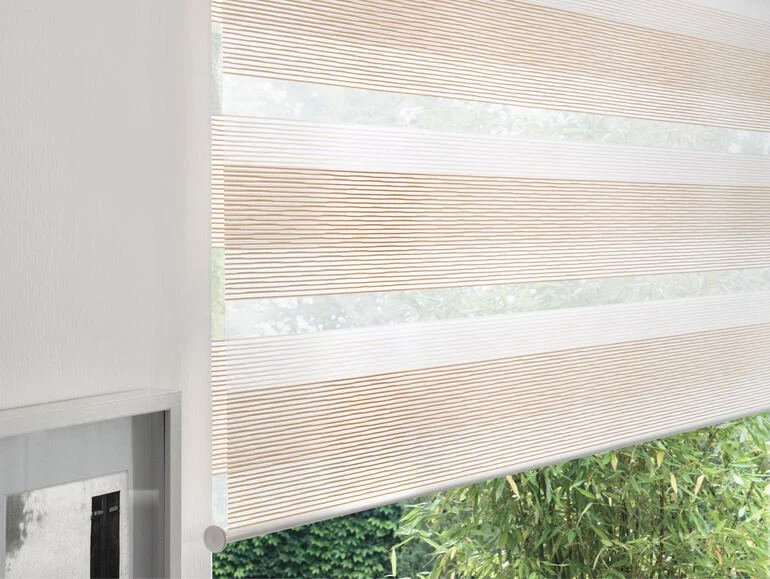 Innenraum mit halbtransparentem Rollos, die auf ein Fenster oder Glastür vor einem Garten mit Bäumen und Sträuchern gefallen sind.