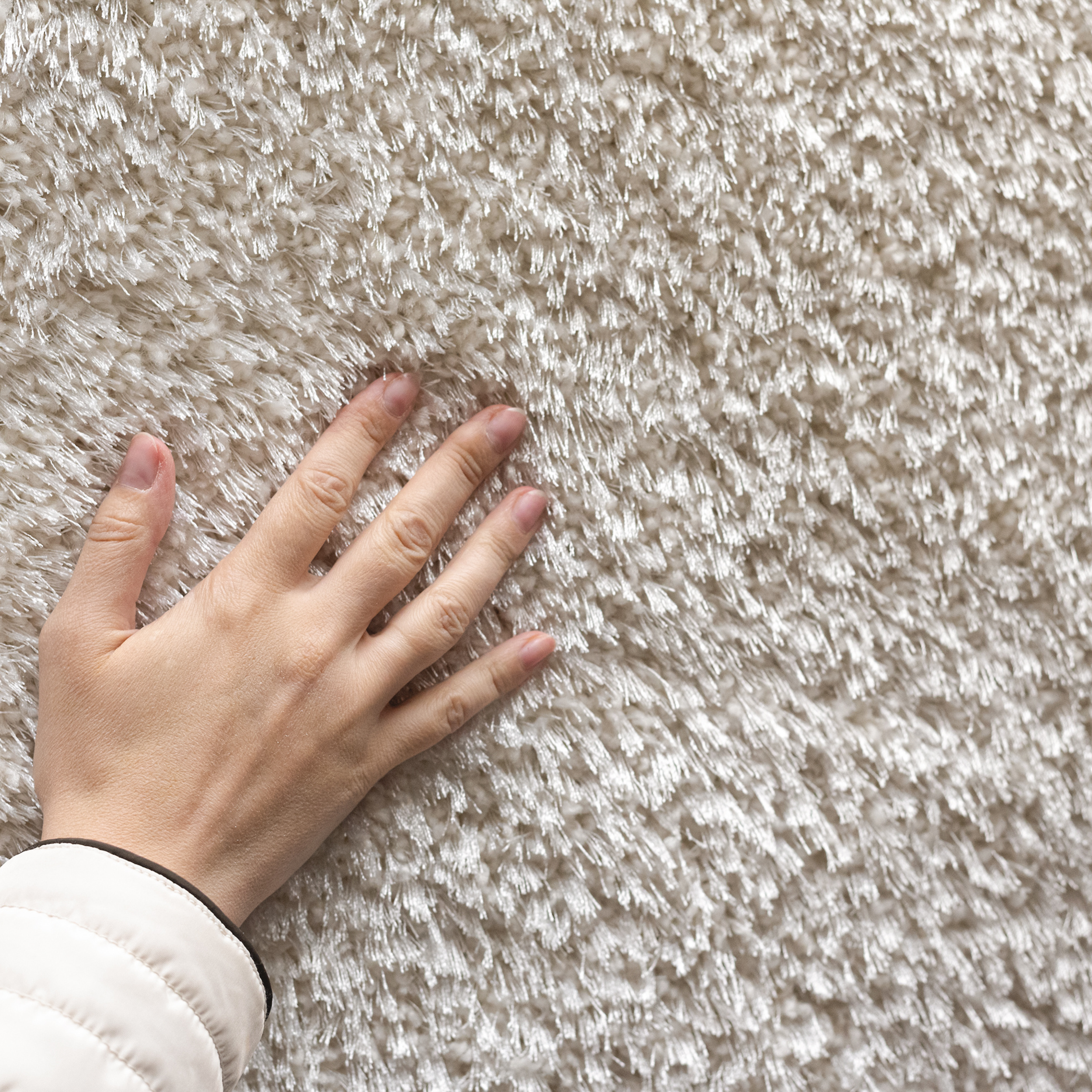 Nahaufnahme von einer Hand, die eine beige, pelzartige Textur eines weichen Teppichs oder Stoffes berührt.