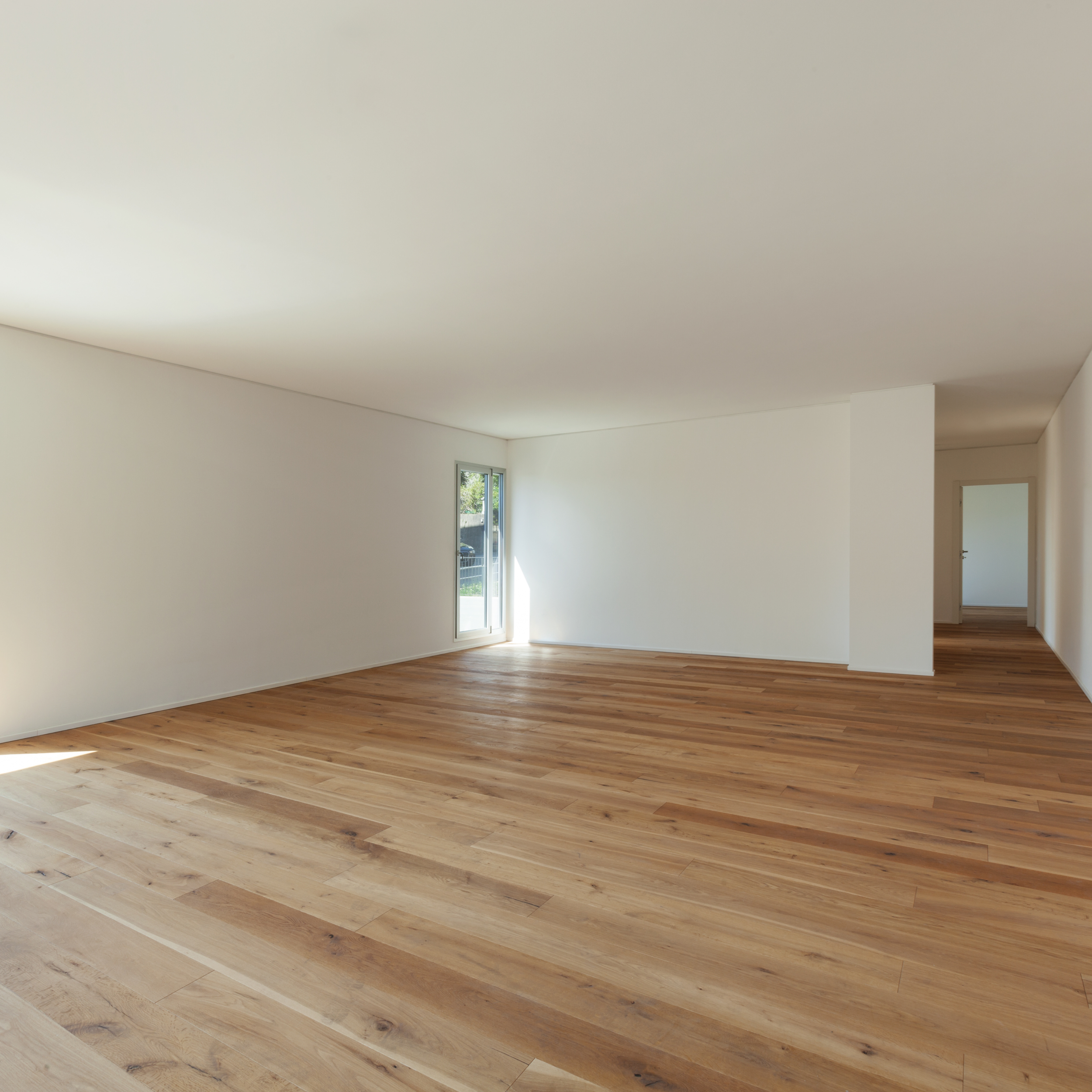 Leeres Zimmer mit Holzfußboden, weißen Wänden, einem Fenster und einer offenen Tür.