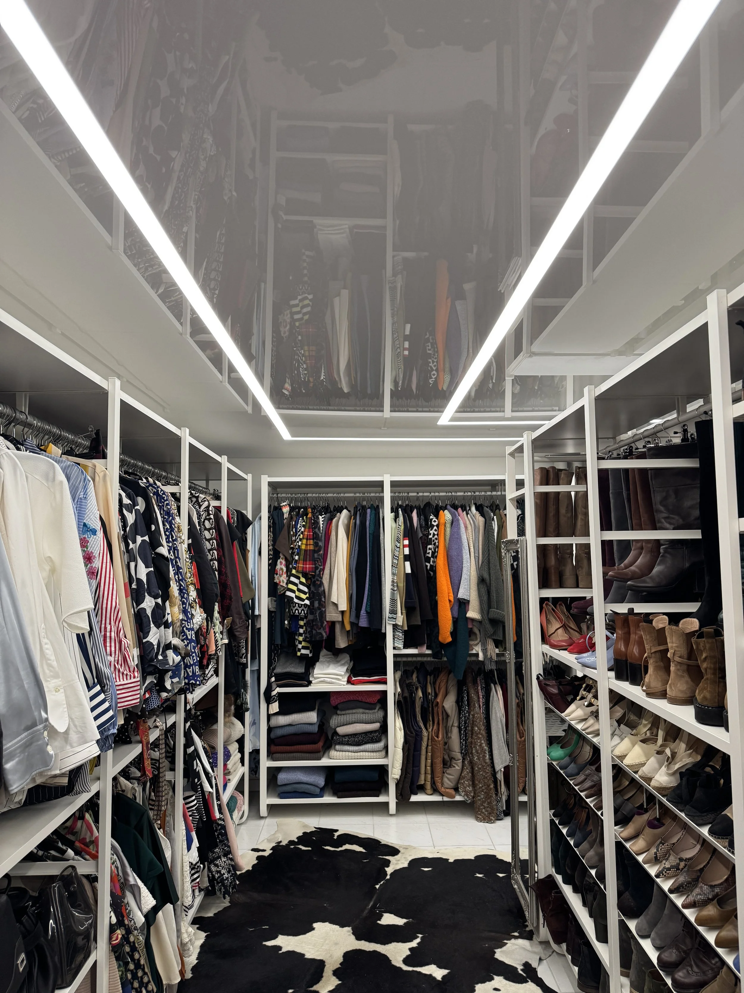 Ein Kleiderschrank mit Kleidung, Schuhen und Accessoires. Es gibt eine schwarze und weiße Tierfellmatte auf dem Boden.