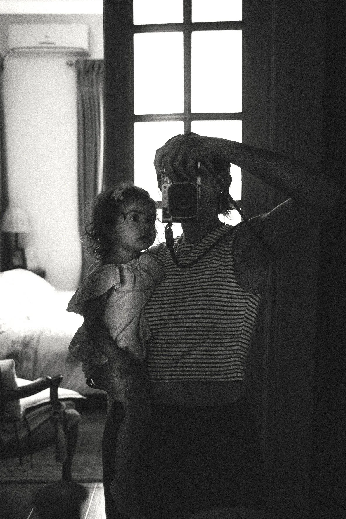 Mother and daughter taking a mirror selfie during a candid family photography session at home in Dubai.