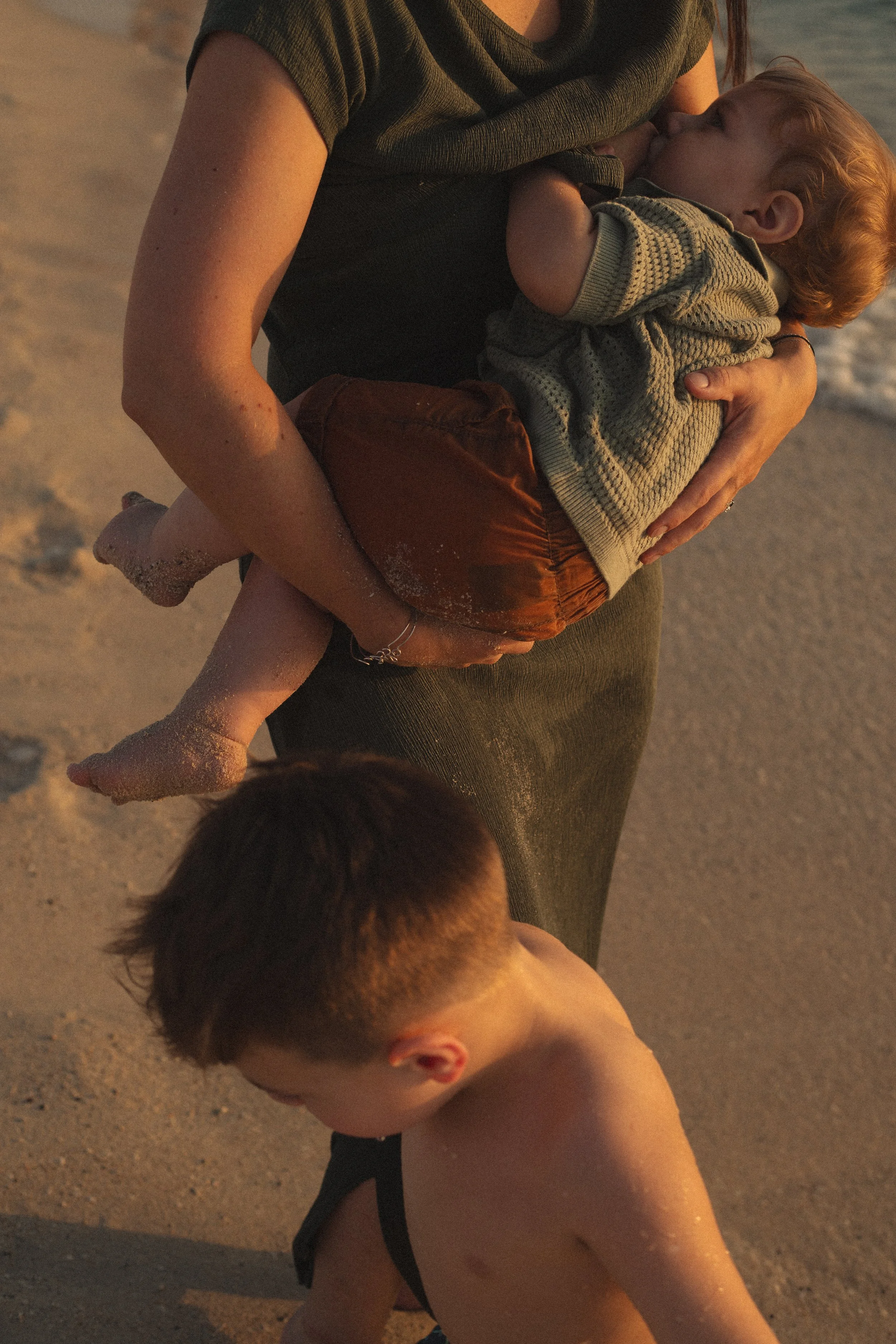 Mother breastfeeding her young child on the beach during a natural family photography session in Dubai.