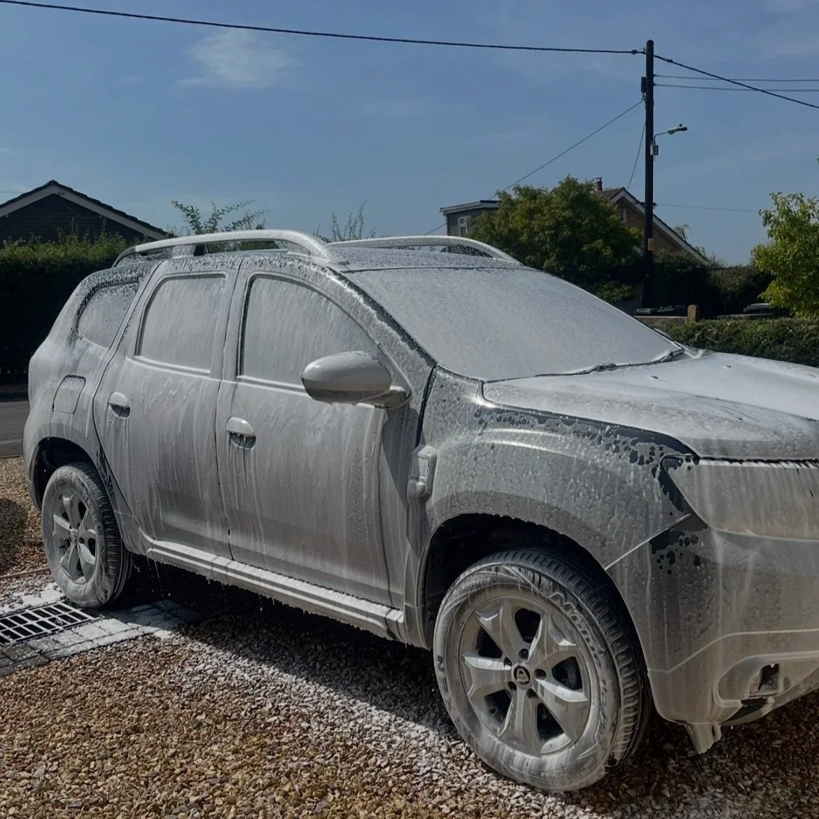 Car covered in soap and foam during a car wash on a sunny day.