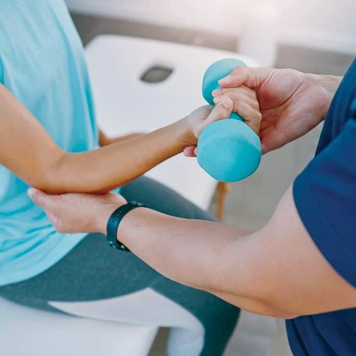Healthcare professional assisting a patient with arm exercises using a small blue dumbbell in a clinical setting.