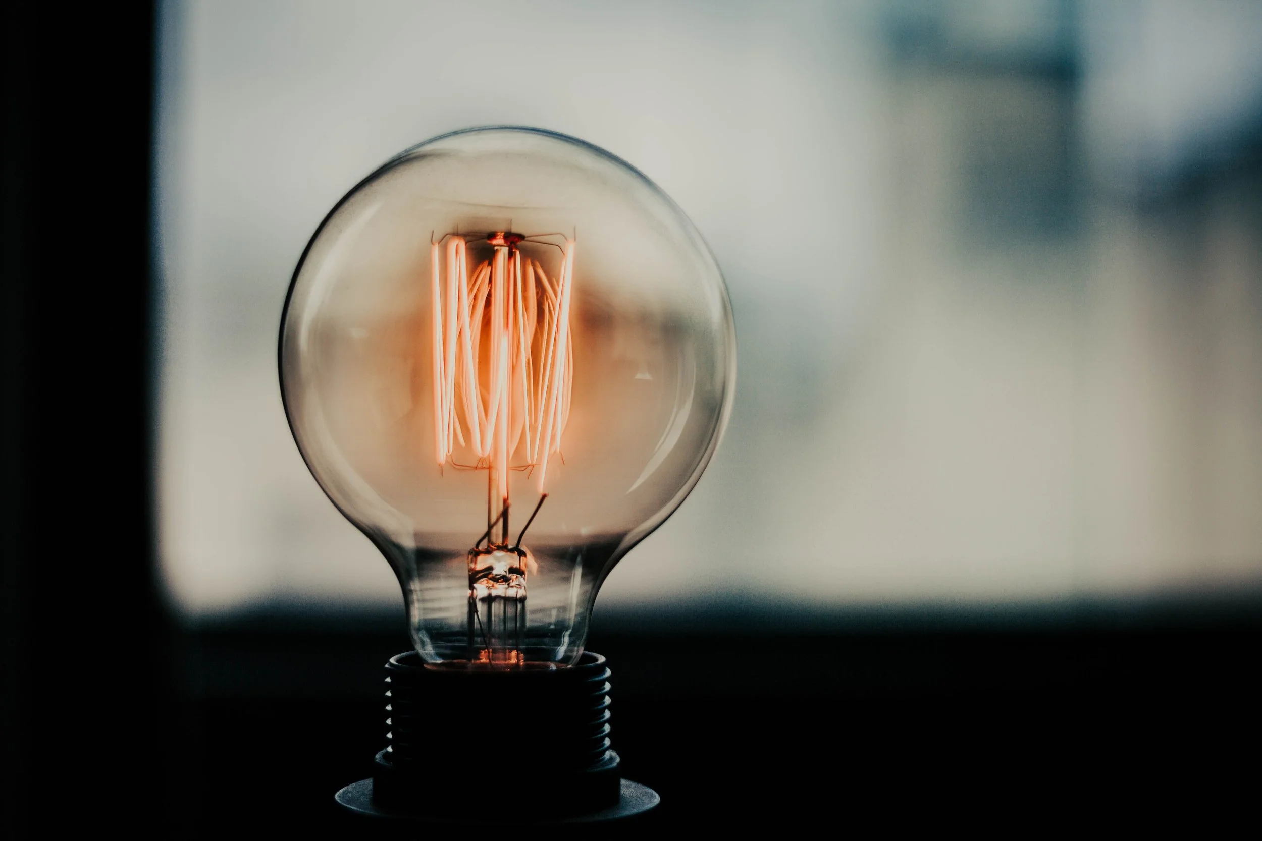 Close-up of an illuminated filament inside a clear light bulb with a dark background.