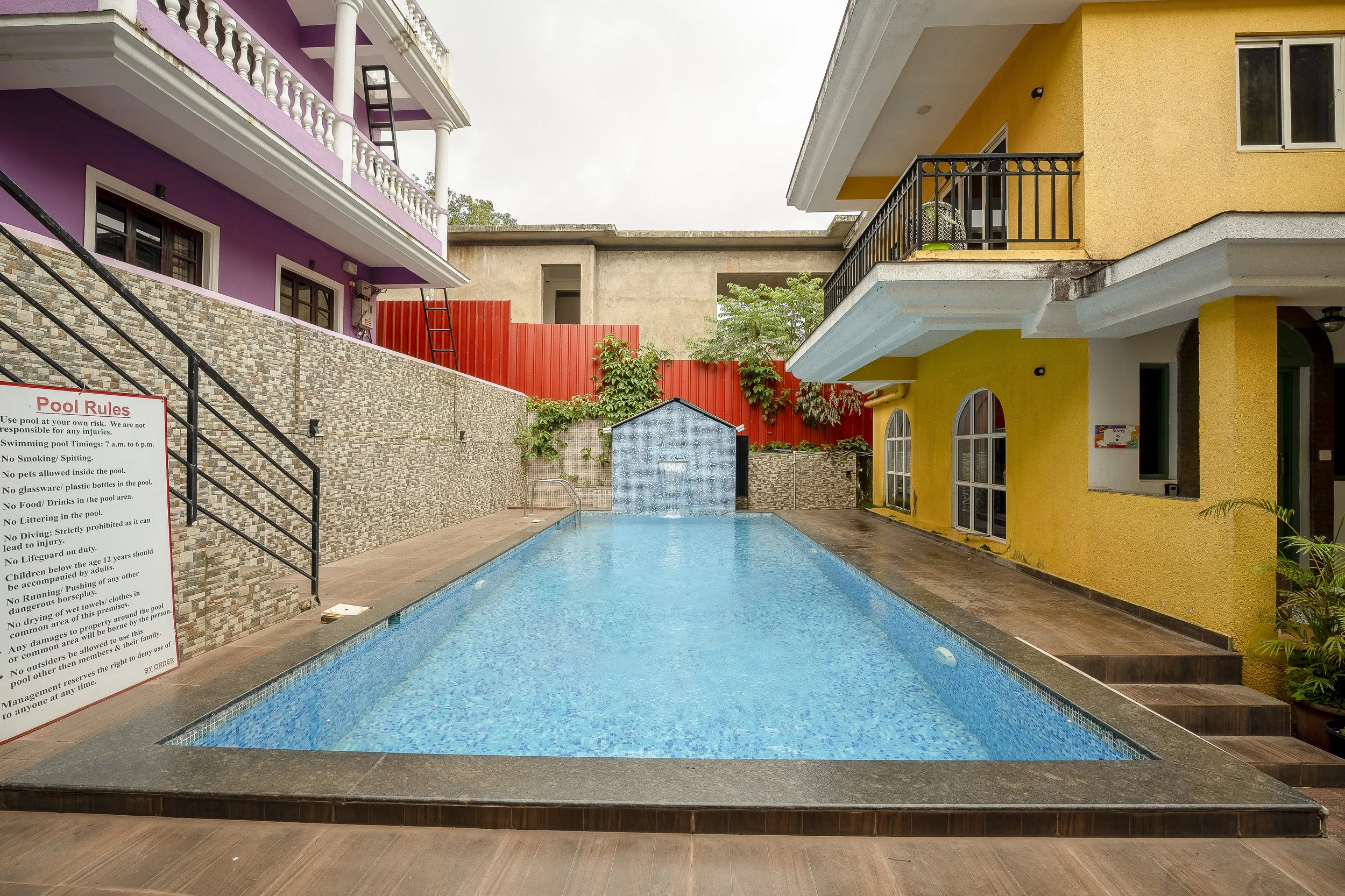 3BHK Villa In Goa With A swimming pool surrounded by colorful buildings, with a sign displaying pool rules.