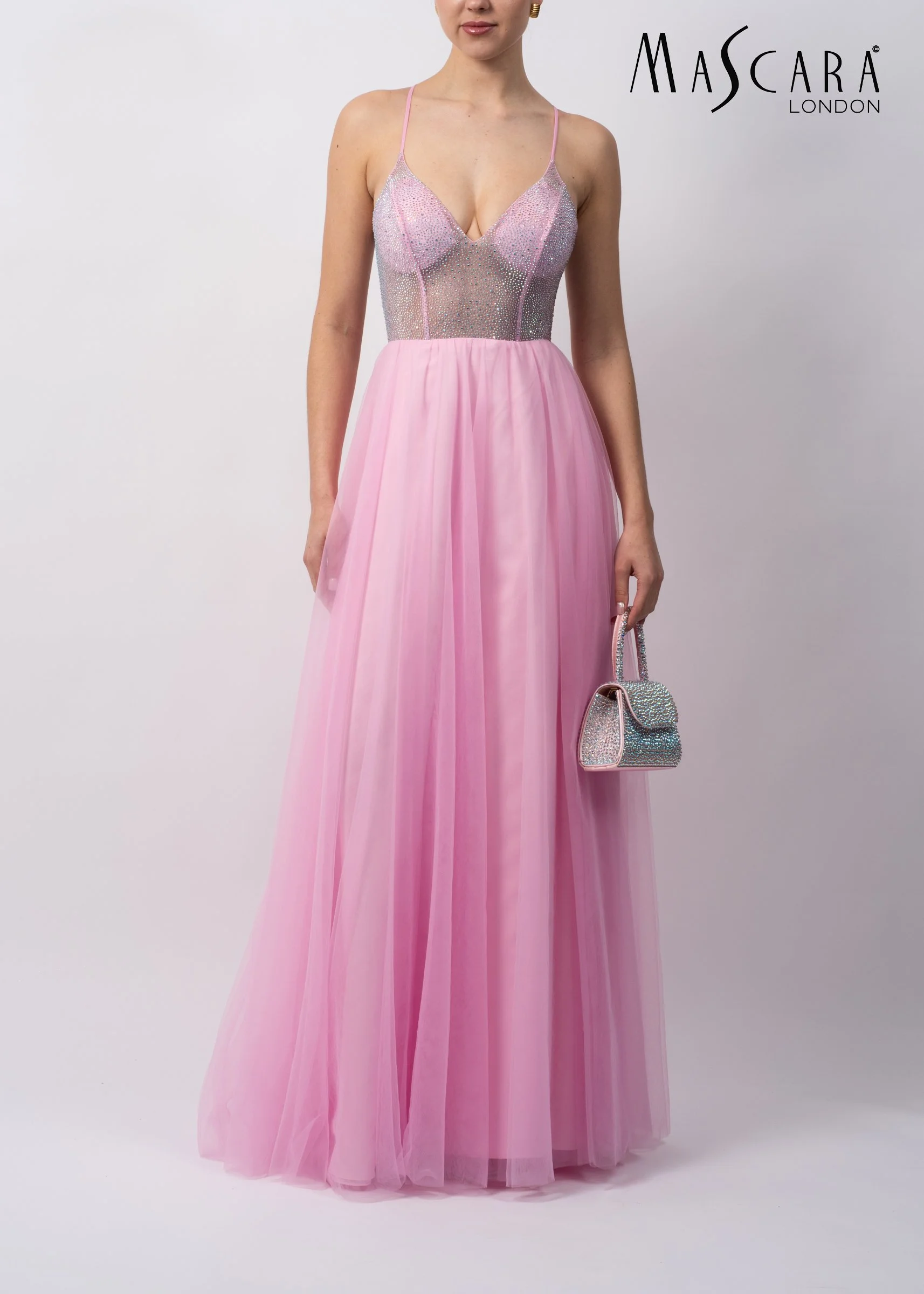 A woman wearing a pink evening gown with a fitted, beaded bodice and a flowing tulle skirt, holding a small matching handbags, standing against a plain white background, with the text 'MASCARA LONDON' in the upper right corner.