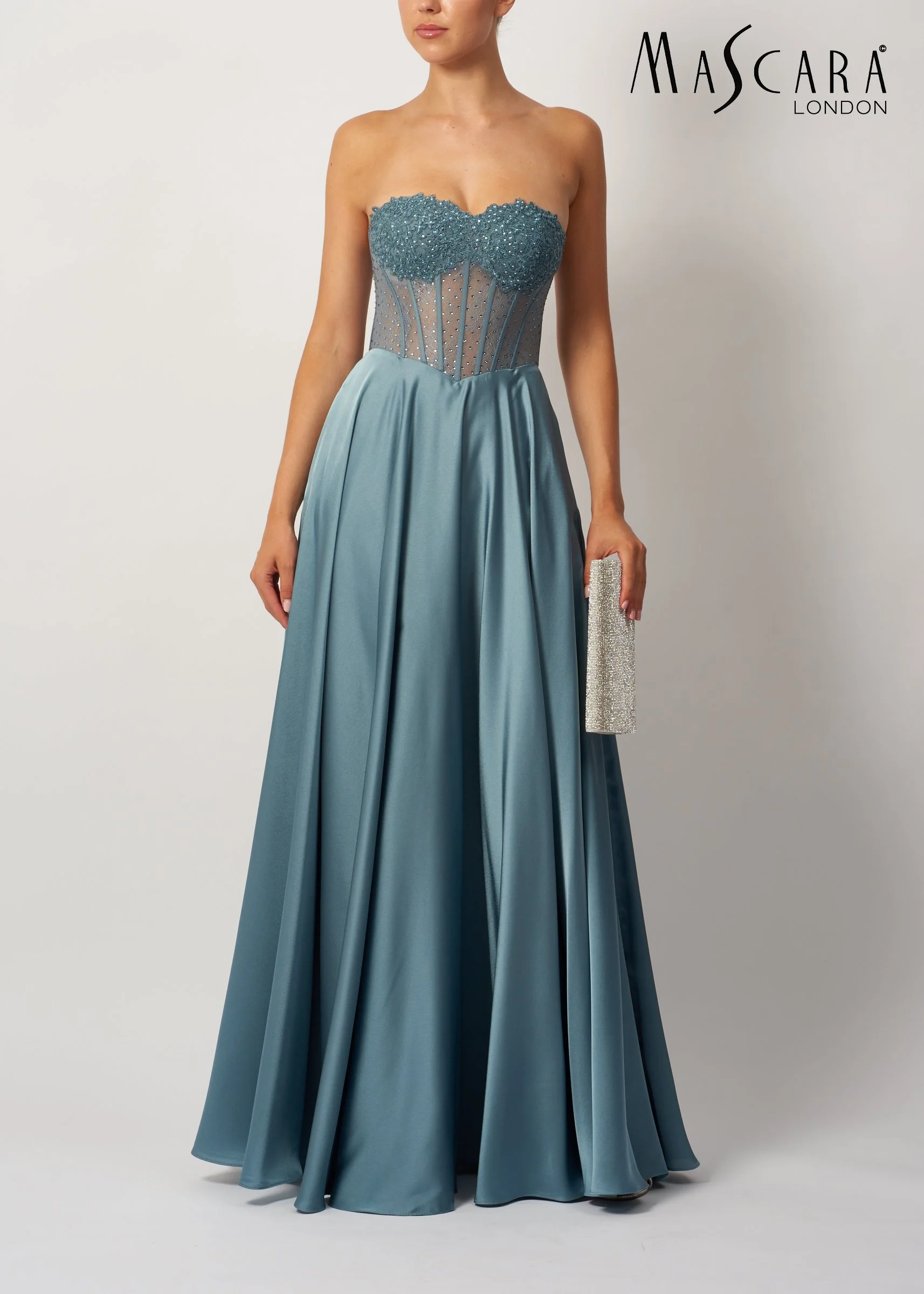 Woman wearing a strapless, blue satin gown with a embellished bodice and full skirt, holding a sparkly silver clutch, standing against a plain white background.