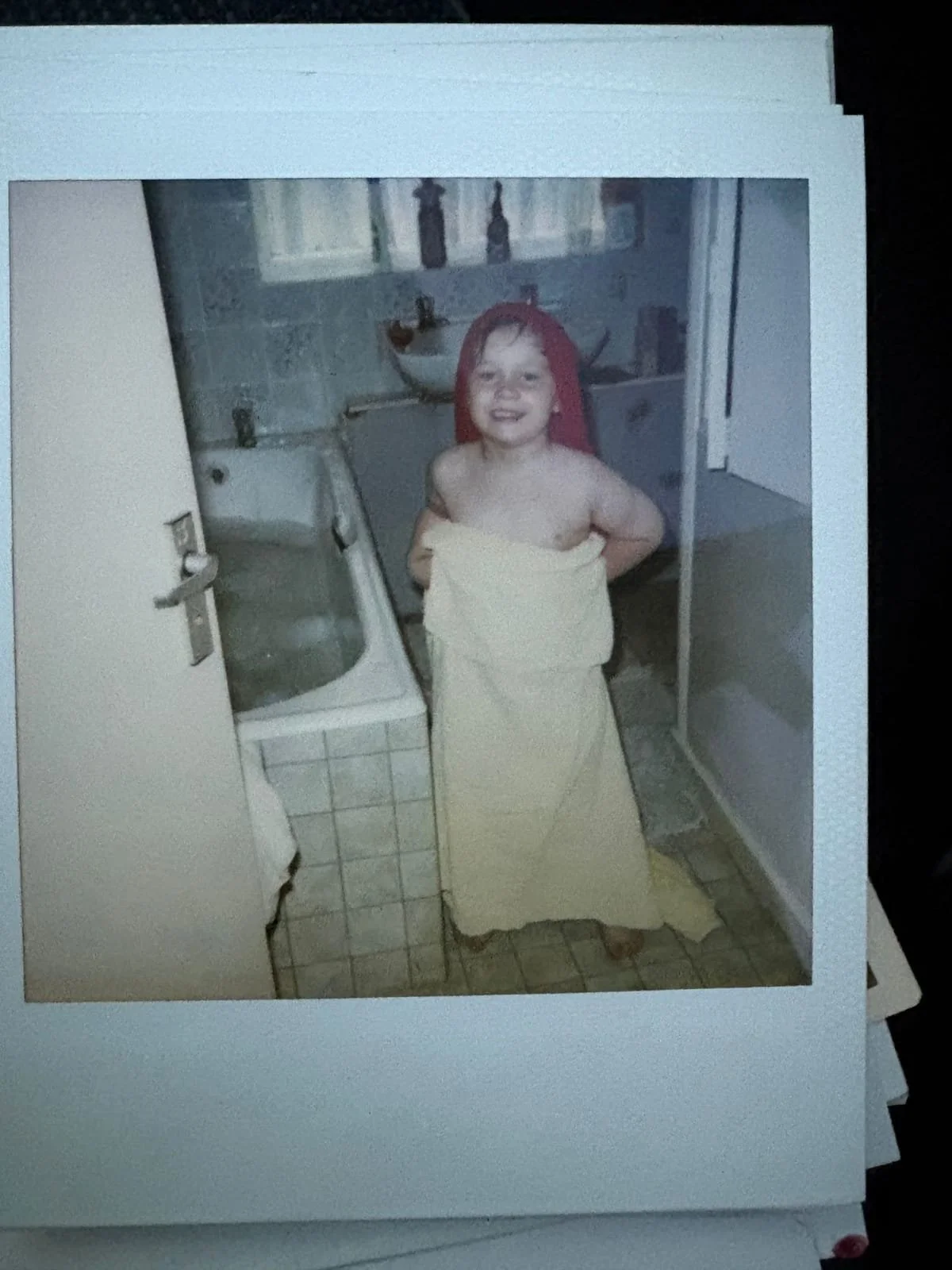 Young child smiling in a bathroom while wrapped in a bath towel after a bath.