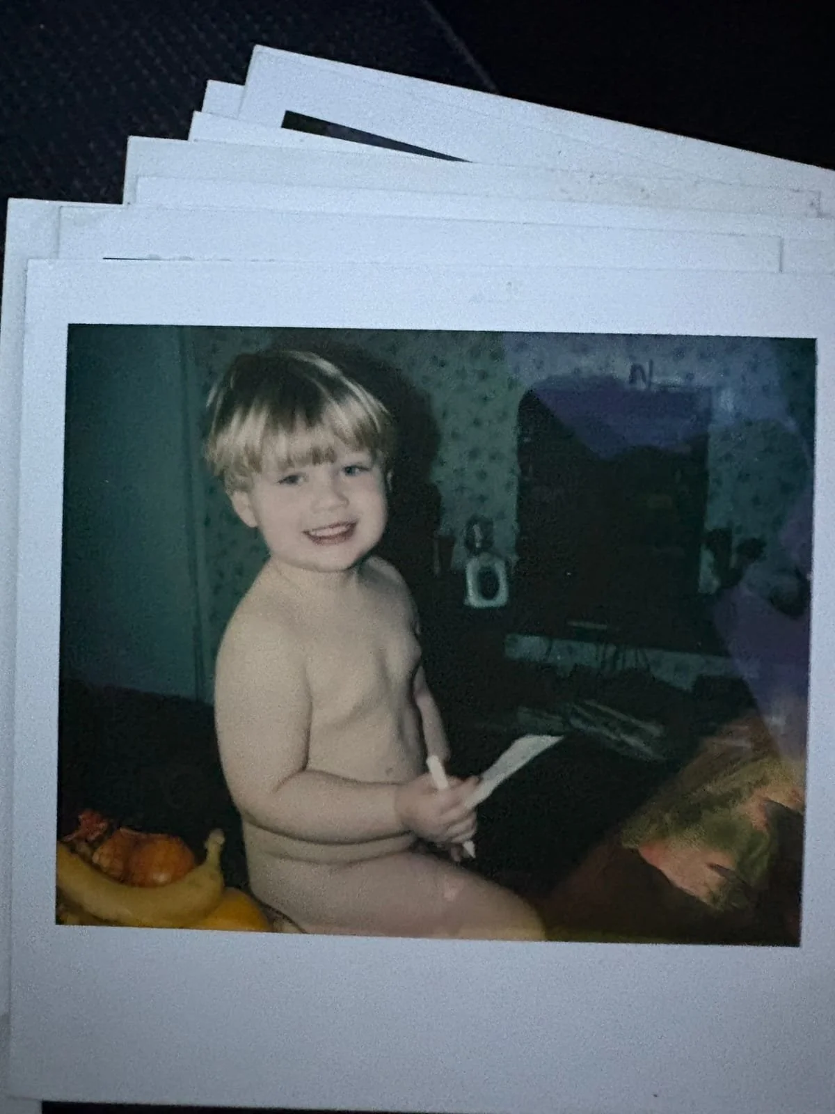 Young child smiling while holding a marker and drawing at home.