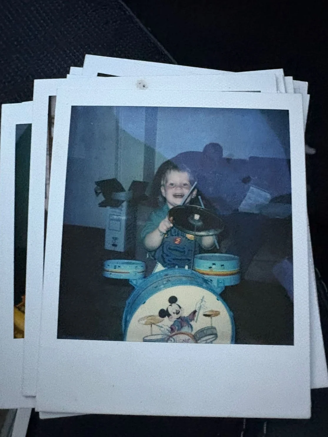 Young child smiling while playing a toy drum kit at home, holding drumsticks with excitement.