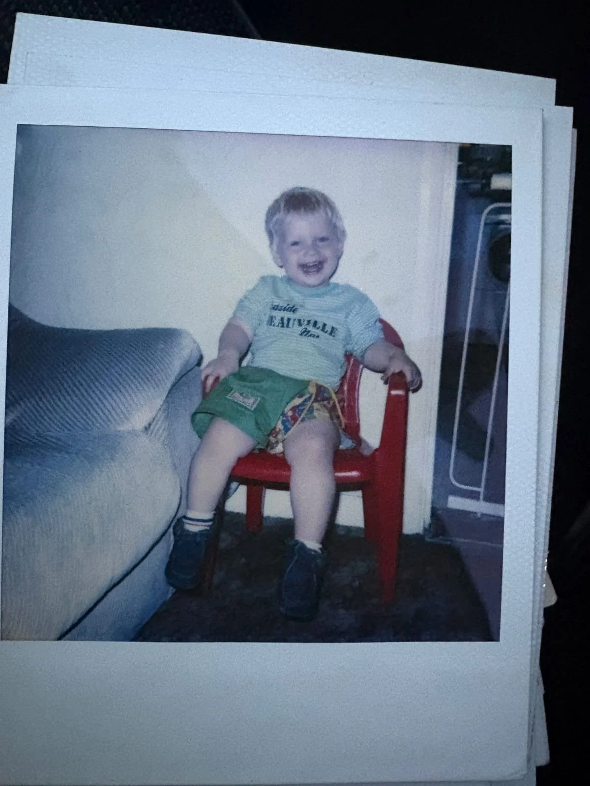 Young child laughing while sitting on a small red chair at home.