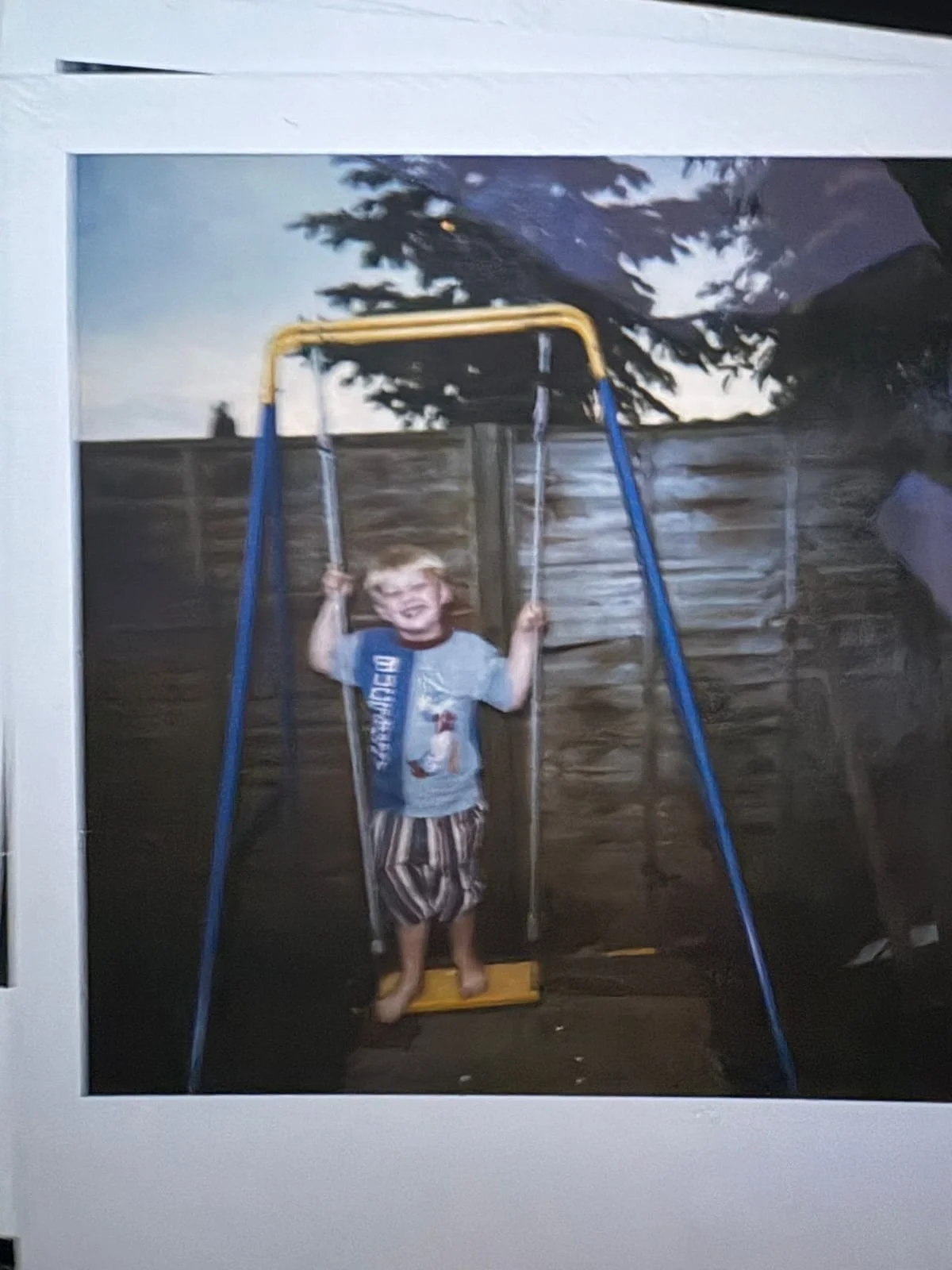 Young child smiling while standing on a garden swing in a back garden.