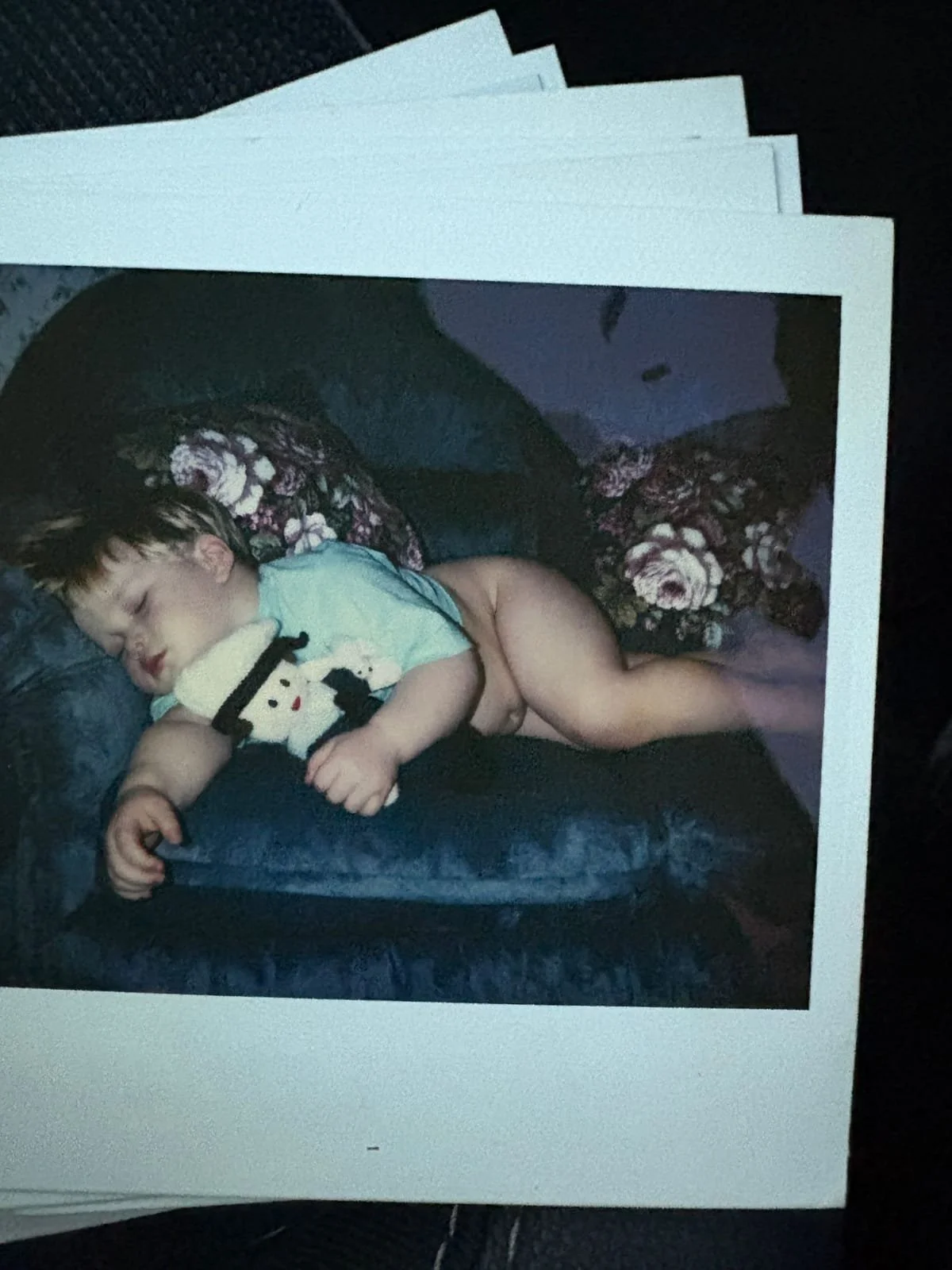 Young child asleep on a blue armchair while cuddling a soft toy.