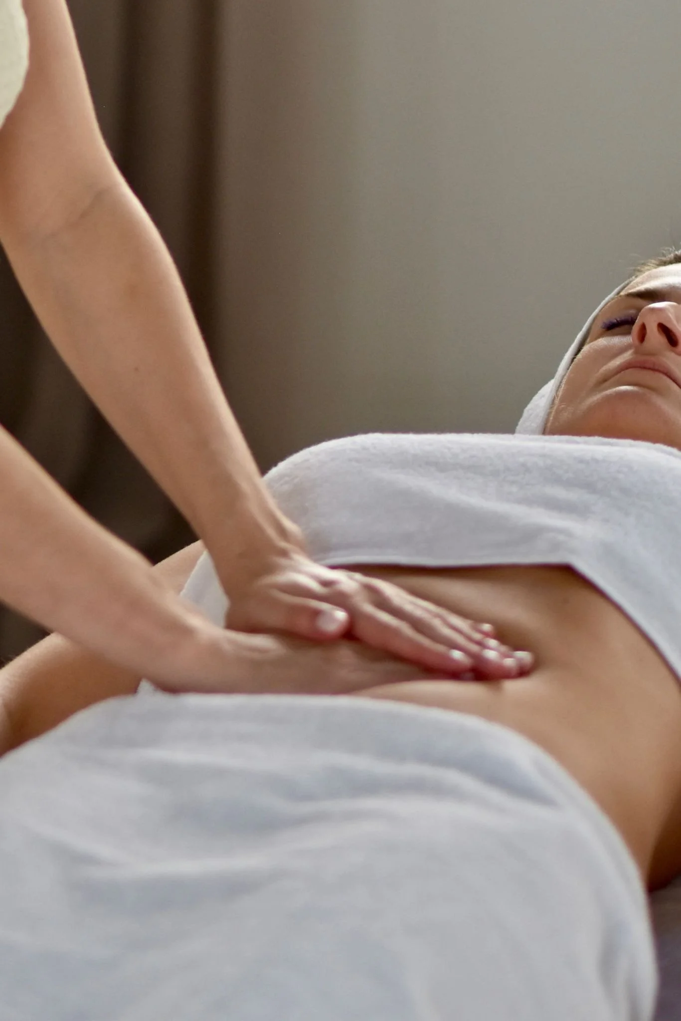 Une personne reçoit un massage, allongée sur une table, avec une serviette blanche sur le corps, tandis qu'une autre personne masse son ventre.