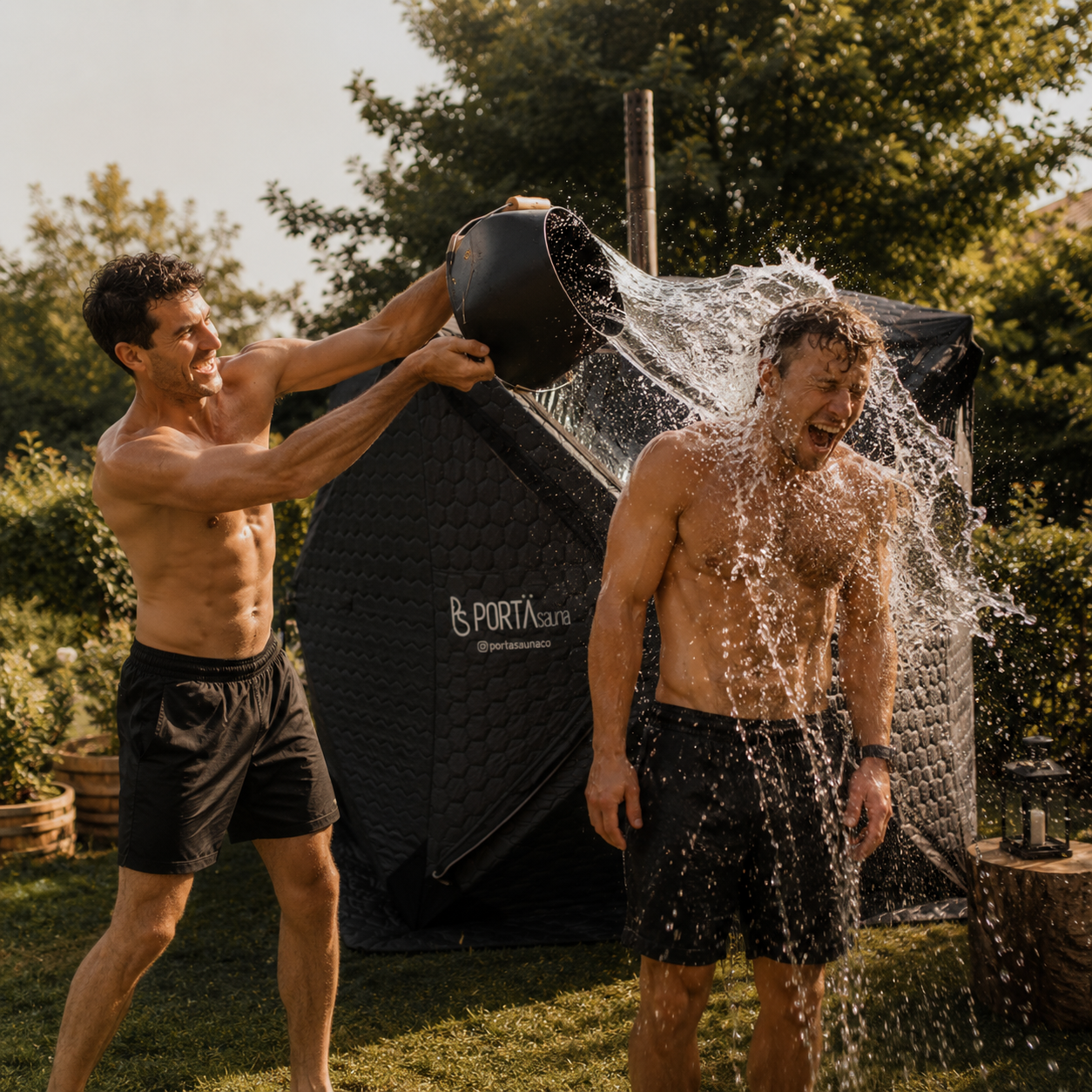 Two shirtless men, one pouring water on the other's head from a black bucket outdoors during daytime, with greenery and a black portable sauna in the background.