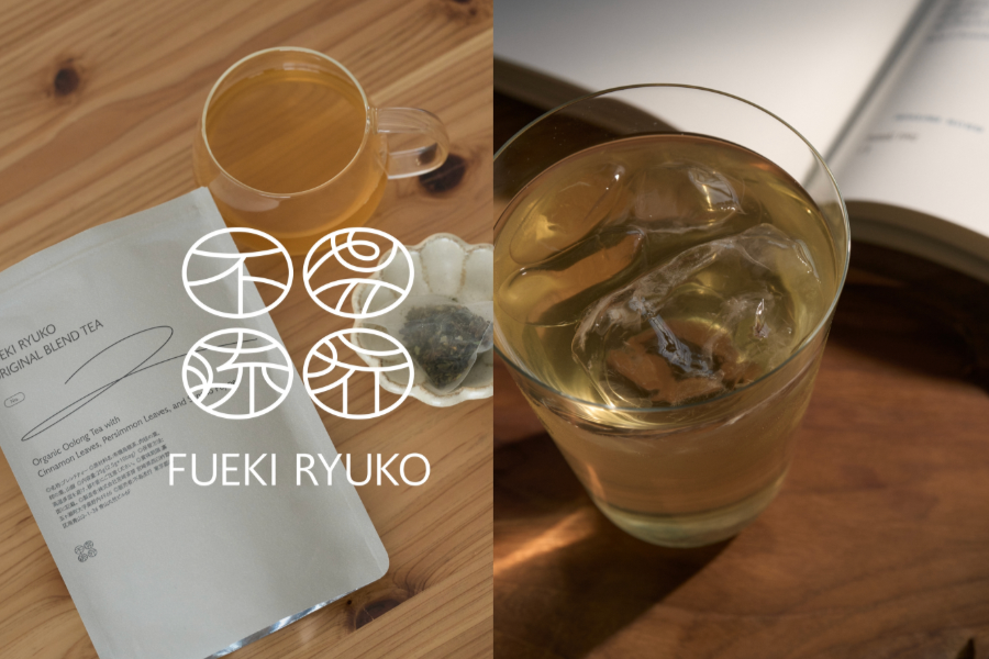 左側に茶色い飲み物が入ったガラスマグカップ、葉っぱの形をした白い皿に石とティーバッグの袋、紙の説明書と木製のテーブル。右側に氷の入ったグラスと開いた本。