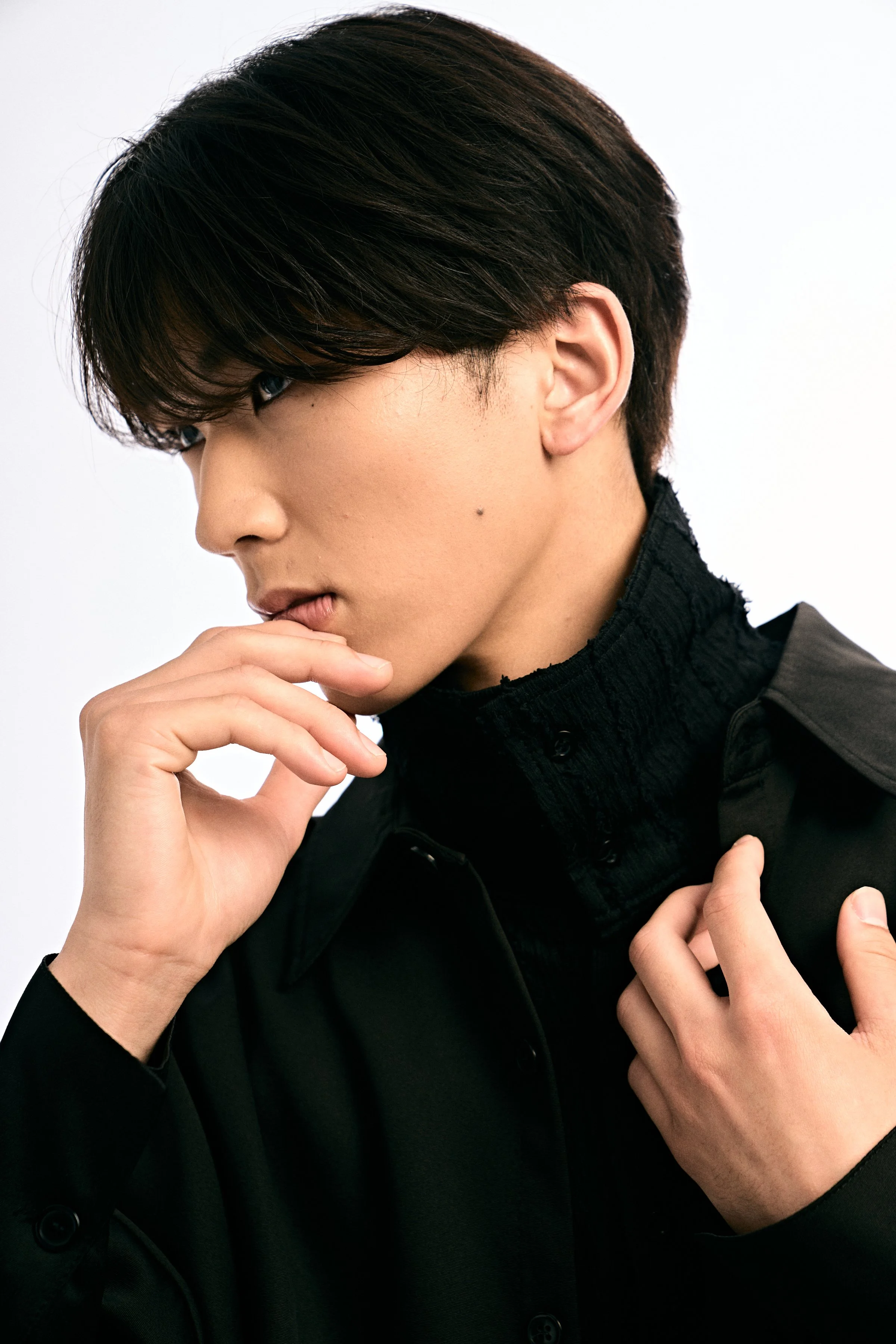 黒い服を着た若い男性が横向きにポーズをとっている写真。白背景。
