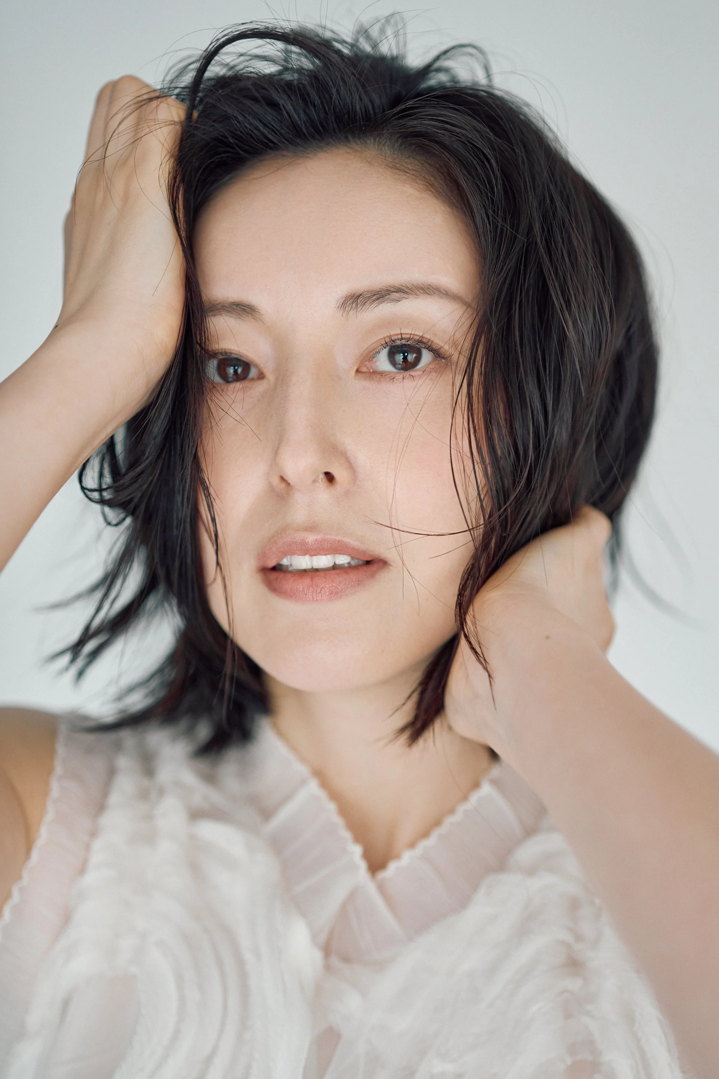 白いレースのトップスを着た女性が髪を触っているポートレート