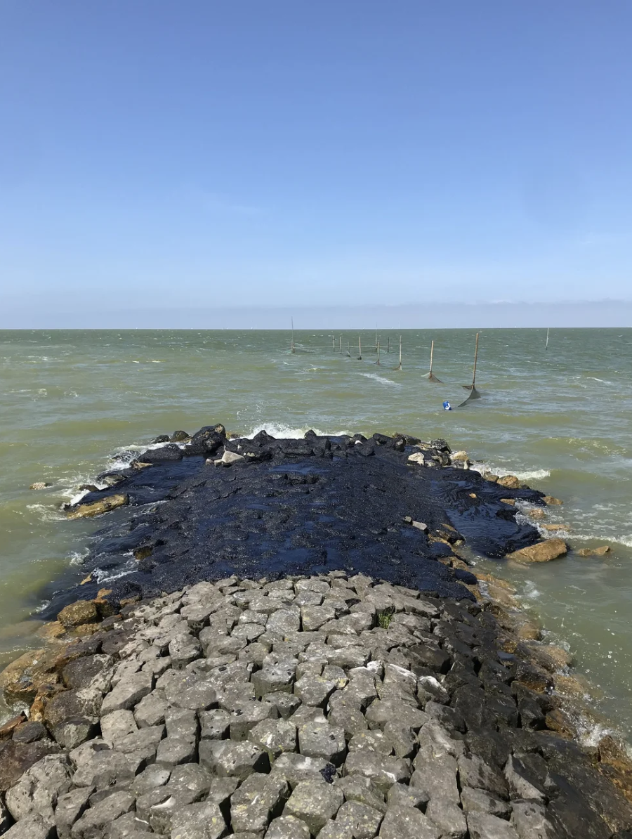 Stenen pier in de zee met golven en een blauwe lucht.