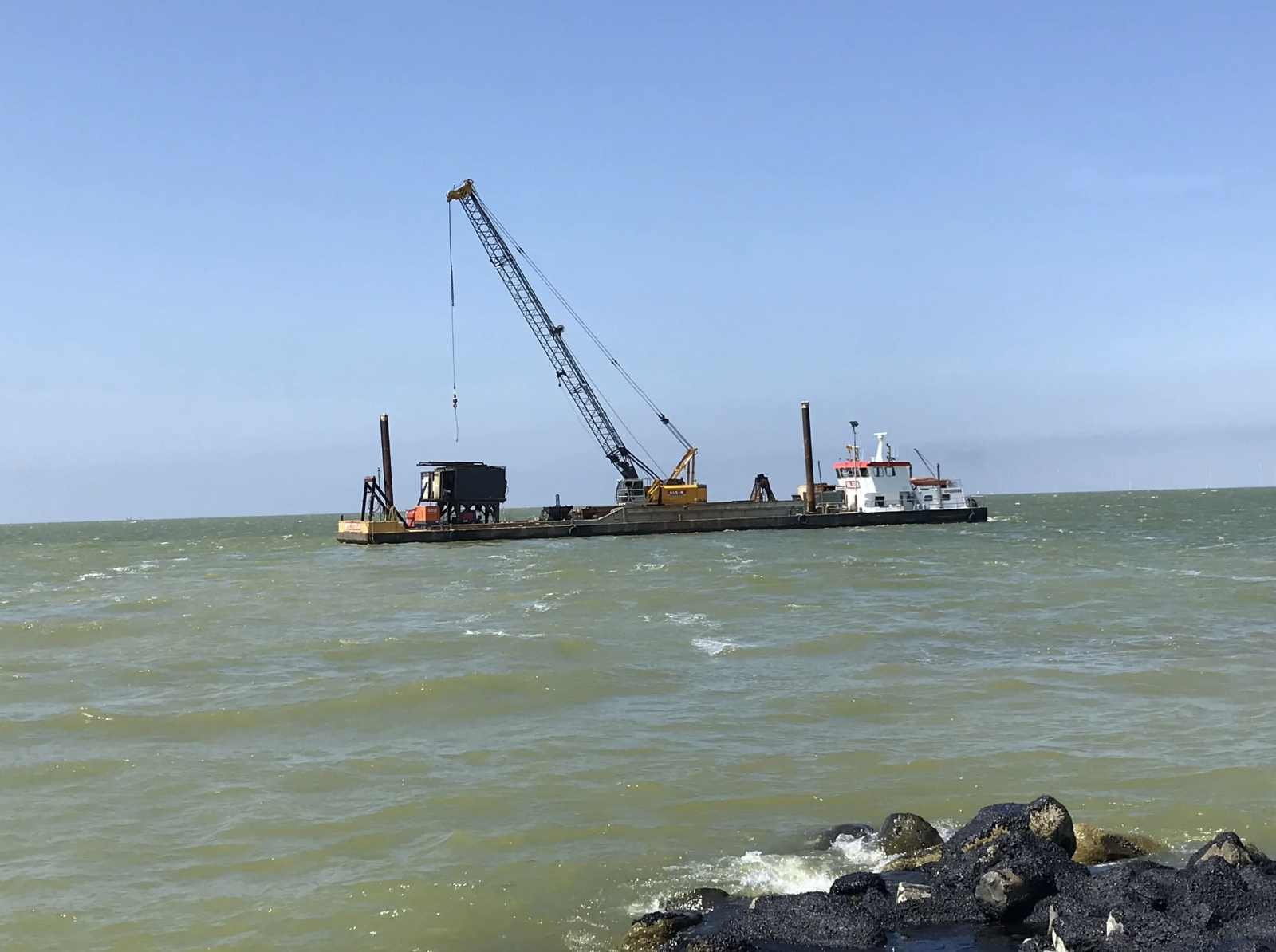 Een werkboot ligt op de zee met een hijskraan en ander werkgerei erop.