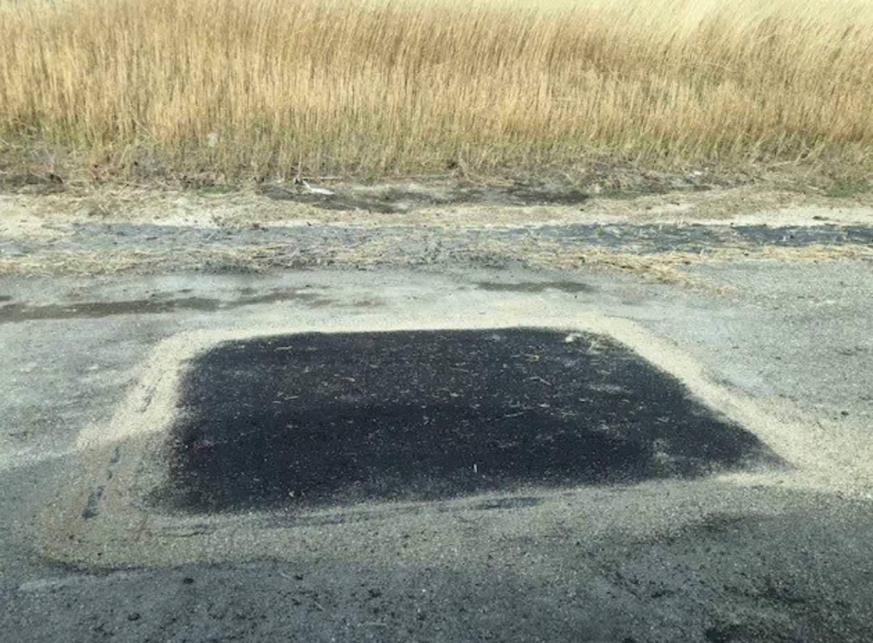 Een wegwerkplaats met een grote put onder het wegdek, omgeven door zand en asfalt.
