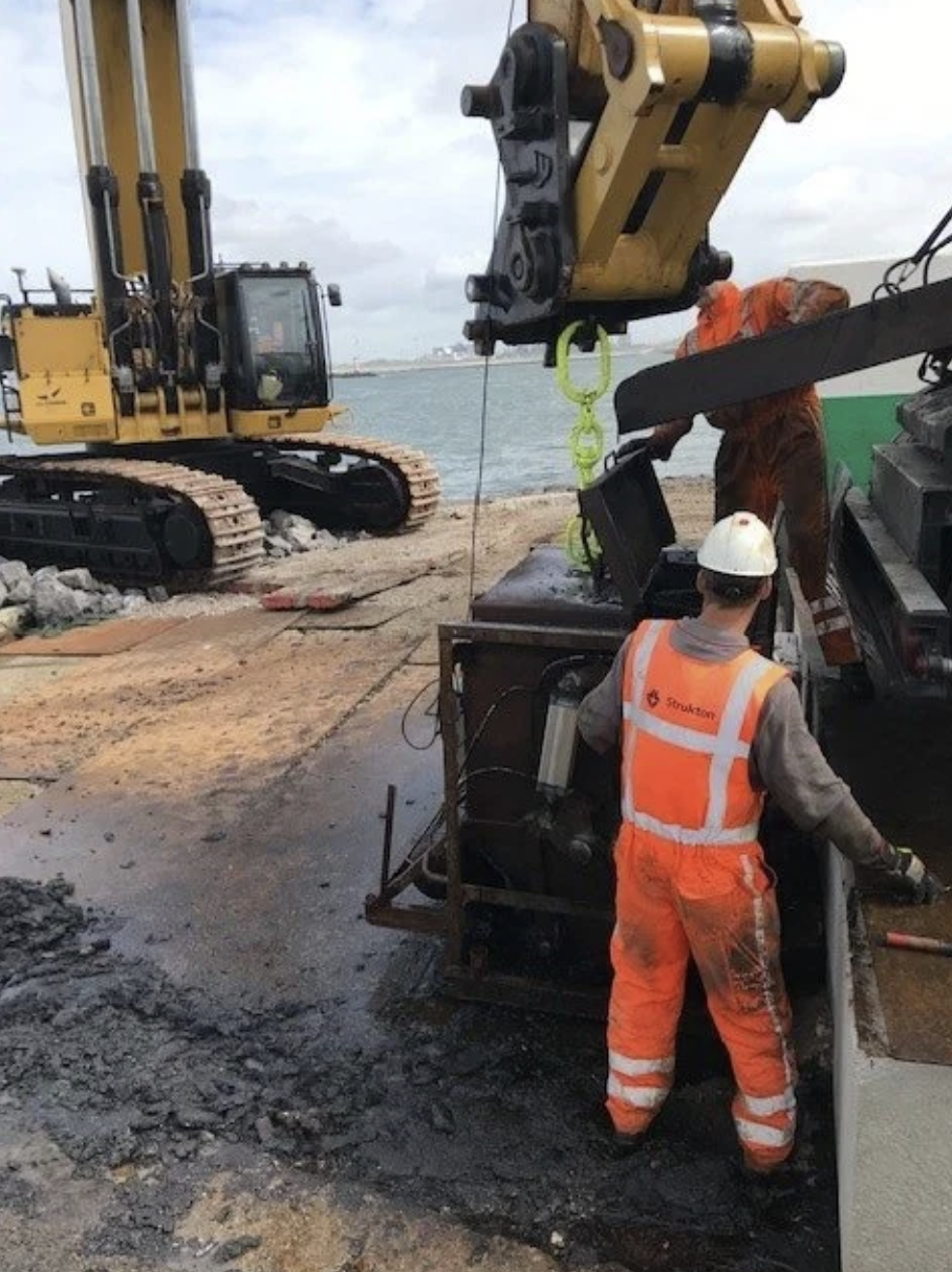 Mensen werken op een bouwplaats bij het water met bouwmachines en veiligheidsuitrusting.