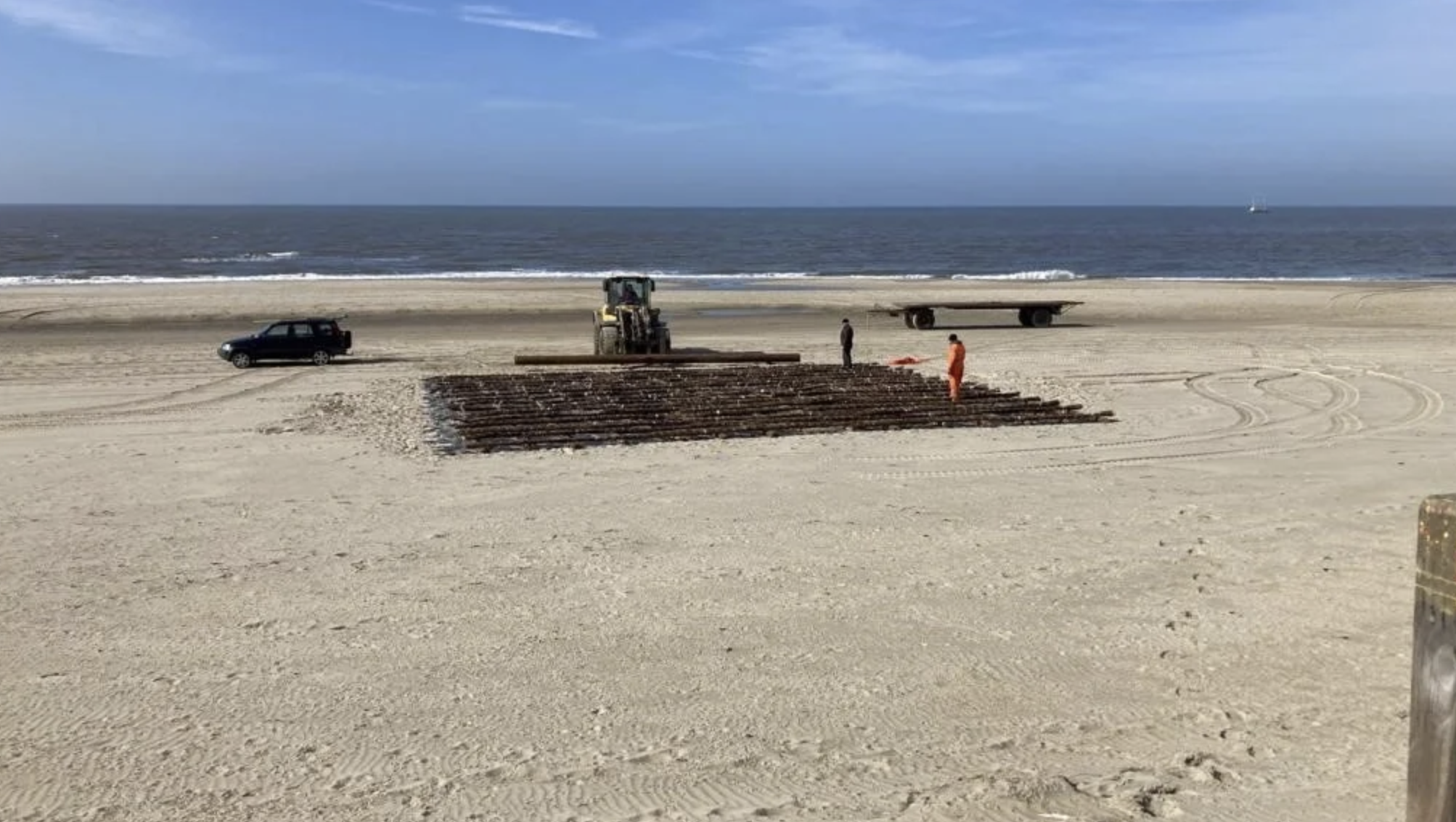 Mensen werken aan een zandsculptuur op het strand, met de oceaan op de achtergrond.