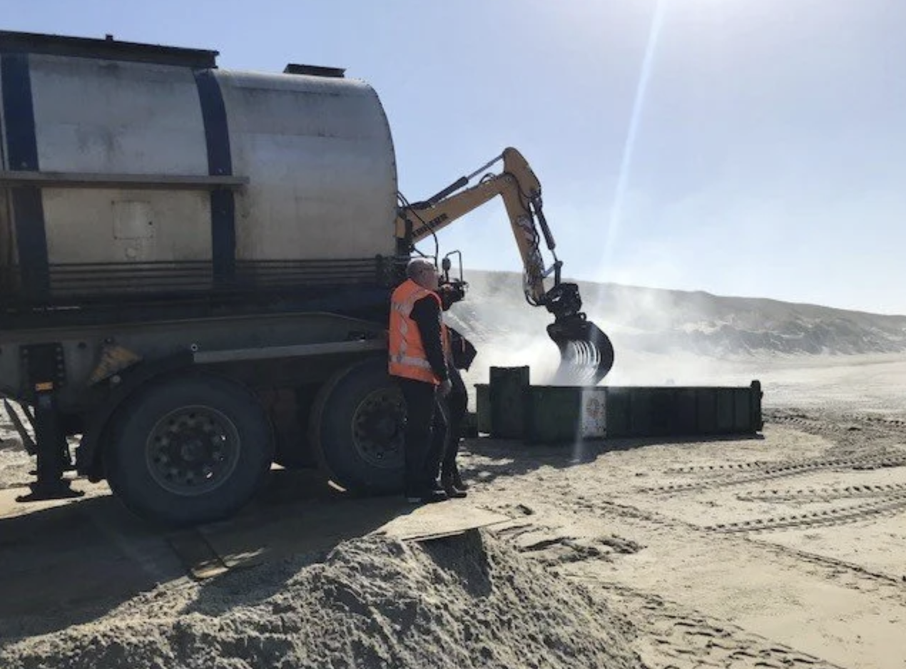 Personeel in veiligheidshesjes die zand bestuurt met een graafmachine op een bouwterrein.