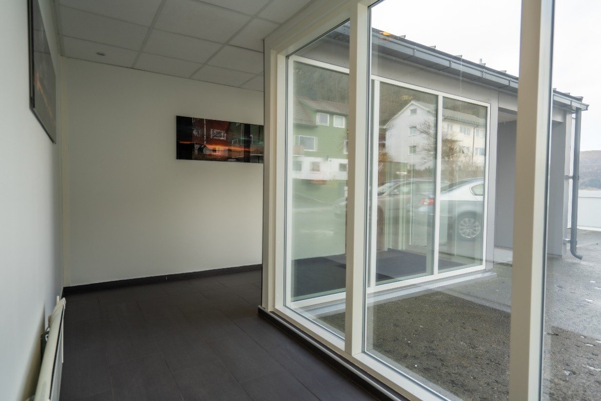 Empty room with large glass windows overlooking parked cars and buildings outside.