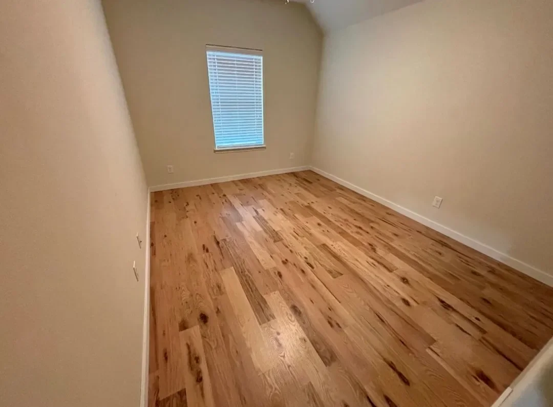 Empty room with hardwood flooring, cream-colored walls, a window with blinds, and baseboards.