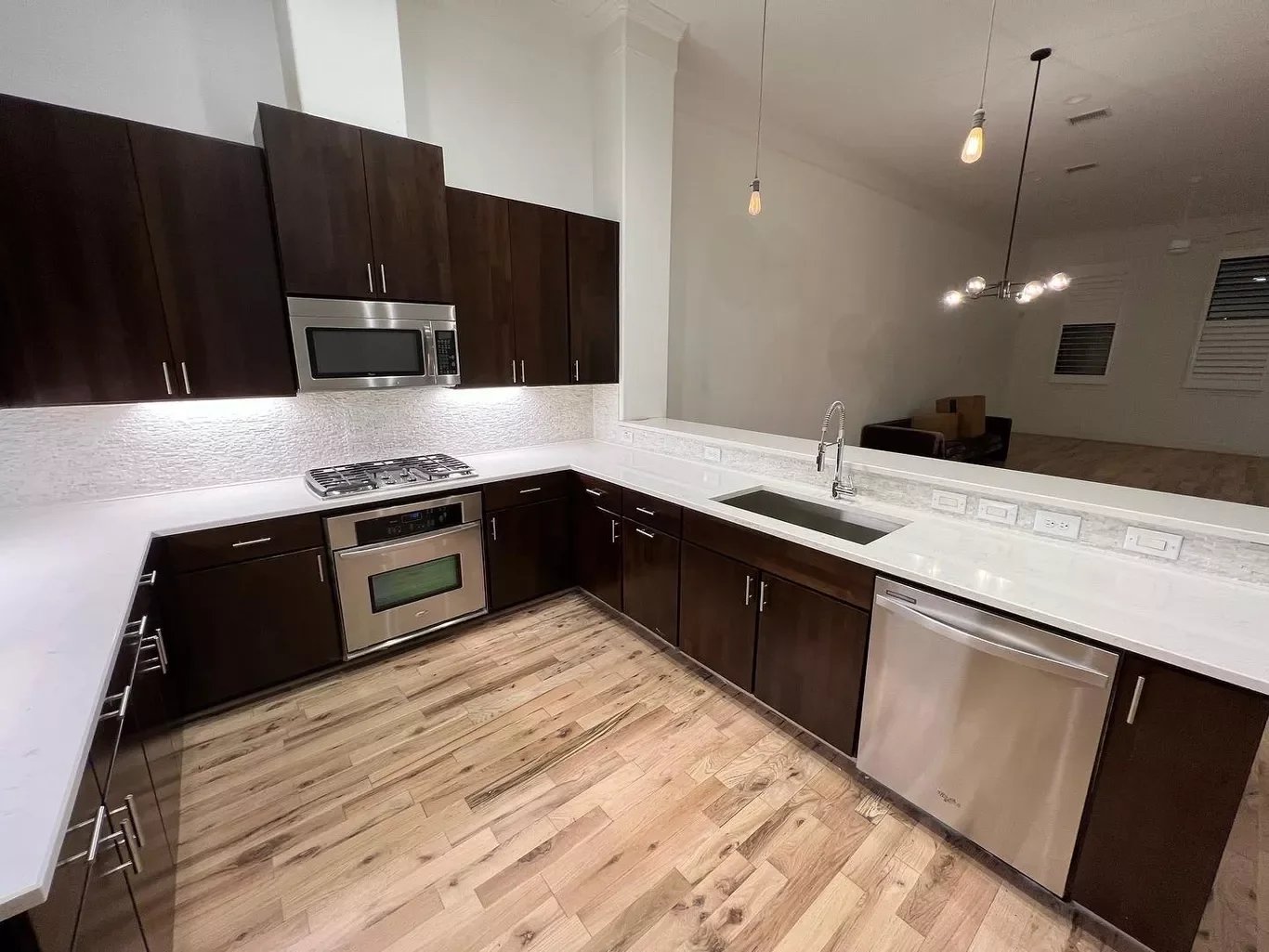 Modern kitchen with dark wood cabinets, stainless steel appliances, white countertops, and hardwood floors.