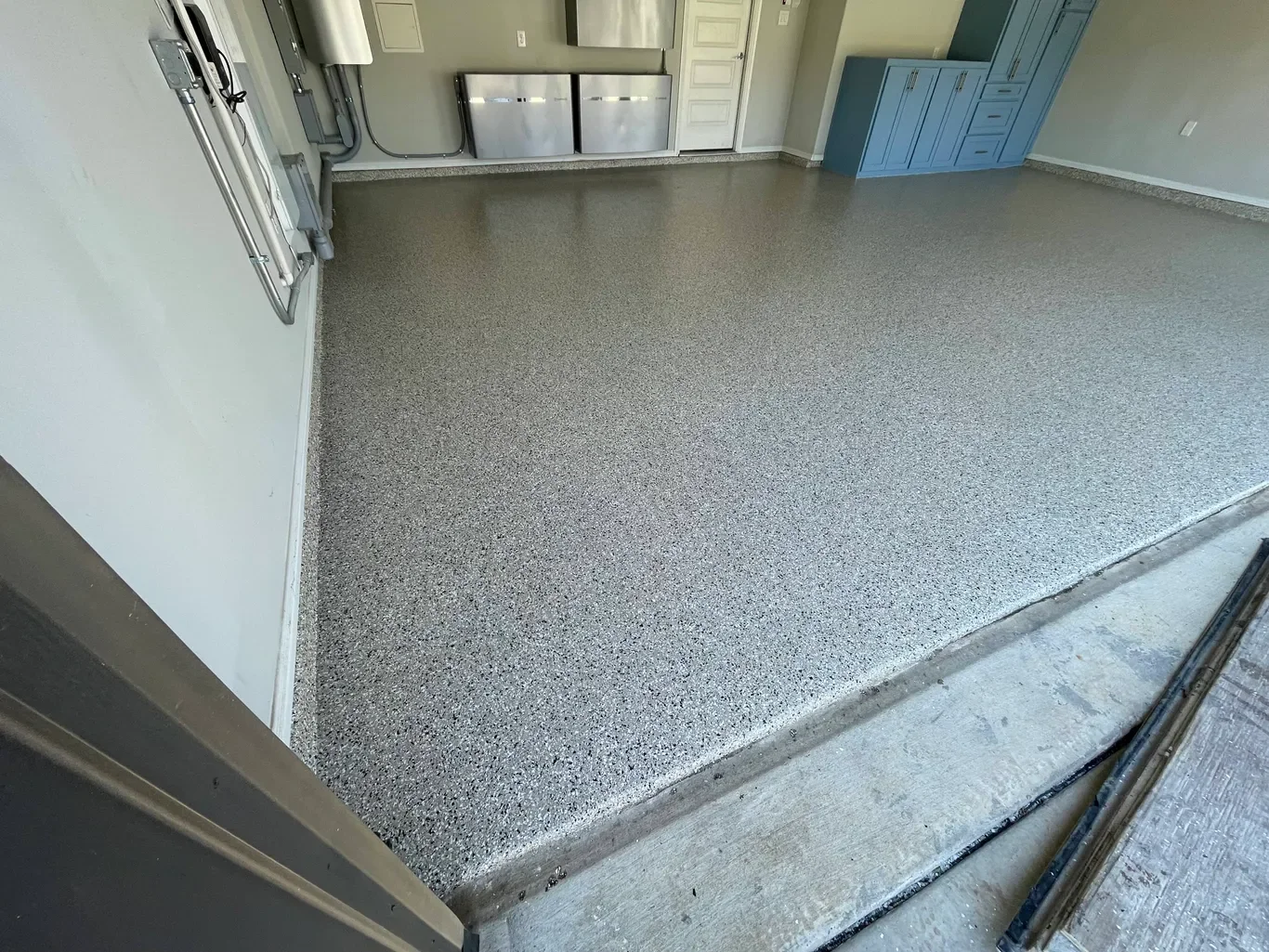 Empty garage with newly installed epoxy flooring, blue cabinets, and utility connections on the wall.
