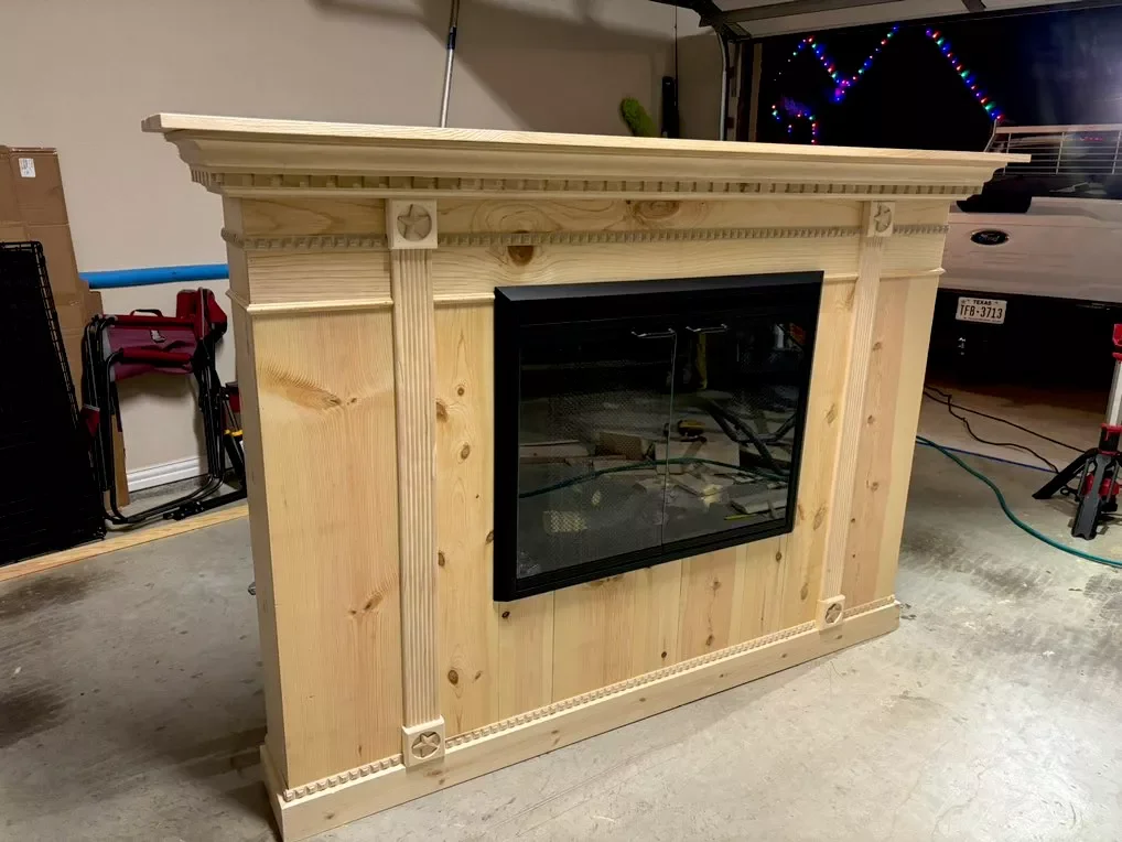 Unfinished wooden fireplace mantel with decorative molding in a garage.