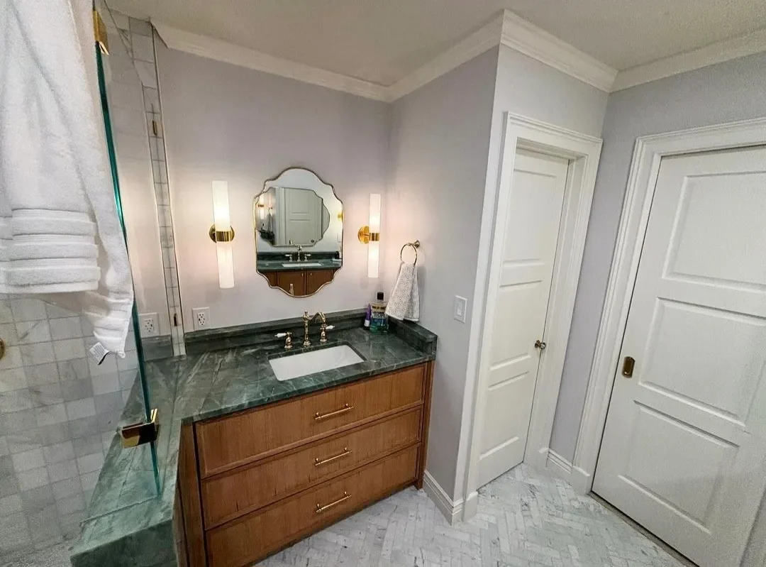 Bathroom vanity with a mirror, sink, and three drawers. There is a wall-mounted towel ring with a towel, and two wall lights on either side of the mirror.
