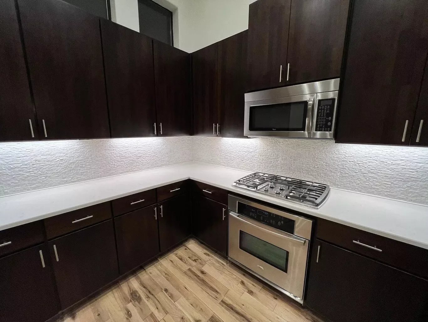Modern kitchen with dark wood cabinets, white countertop, stainless steel microwave, oven, and gas stove, and wood flooring.