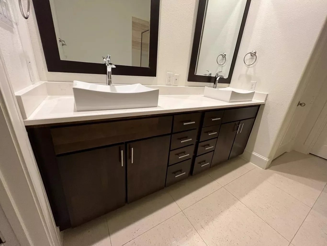 Double bathroom vanity with two rectangular vessel sinks, two mirrors, and dark wood cabinets with silver handles.