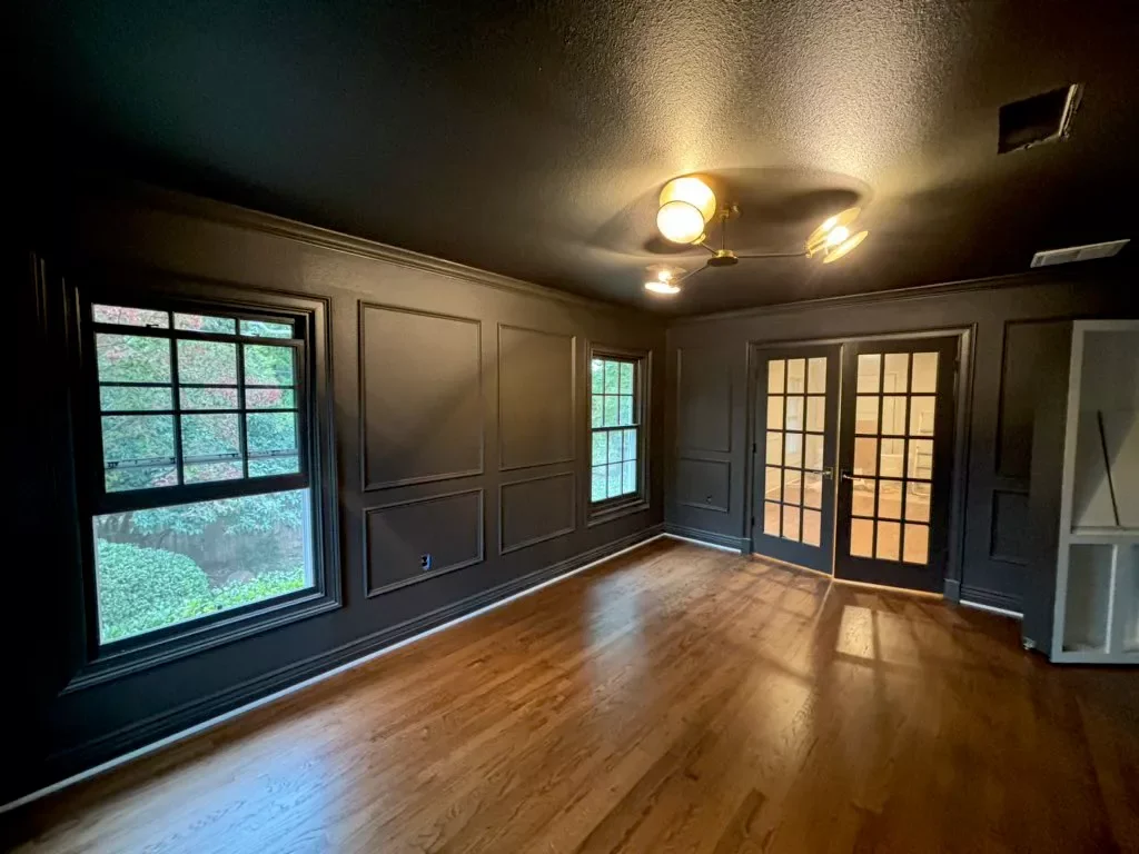 Empty living room with dark gray walls, hardwood floors, two windows, and glass double doors leading outside.